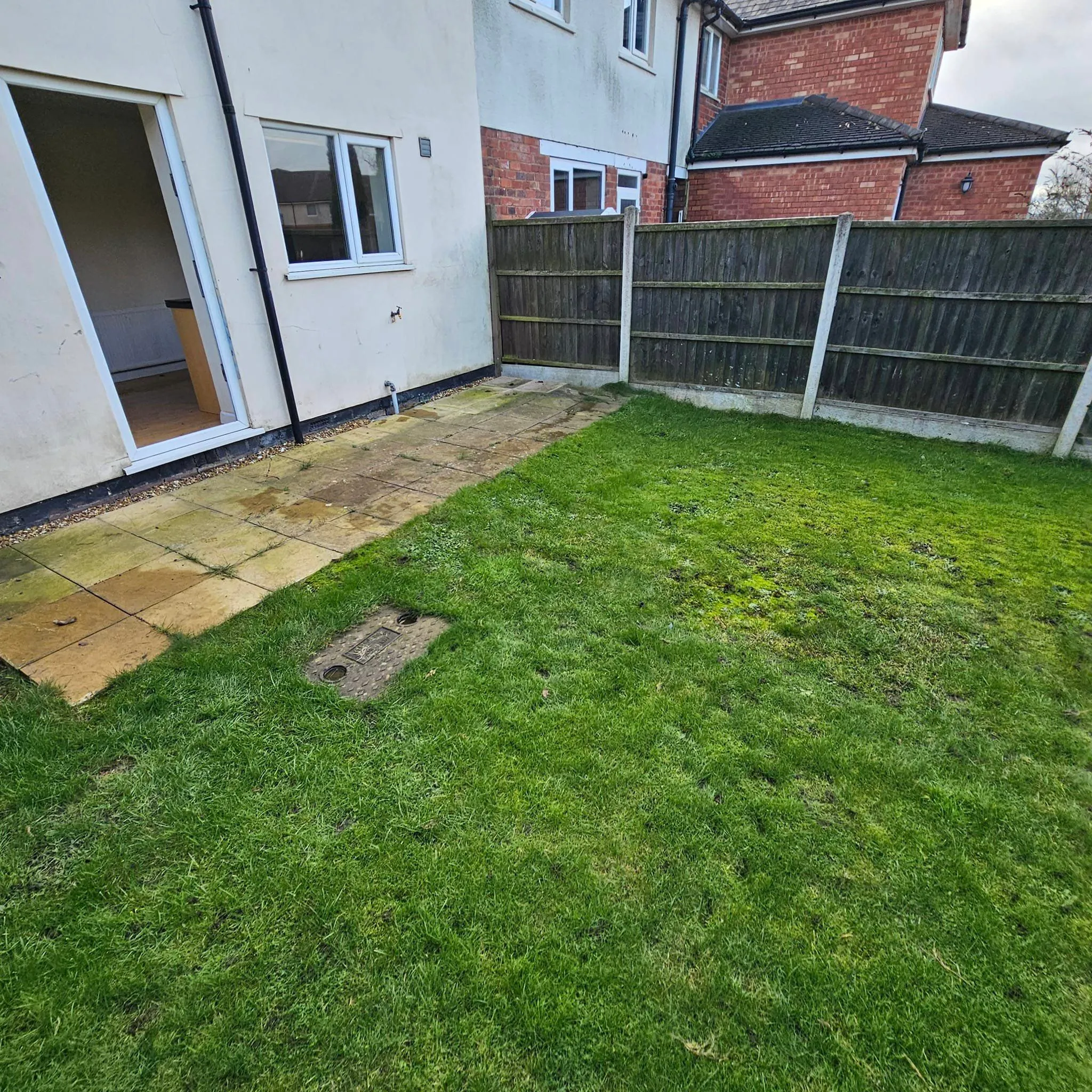 Domestic back garden with mown grass lawn, patio slabs, and timber fence