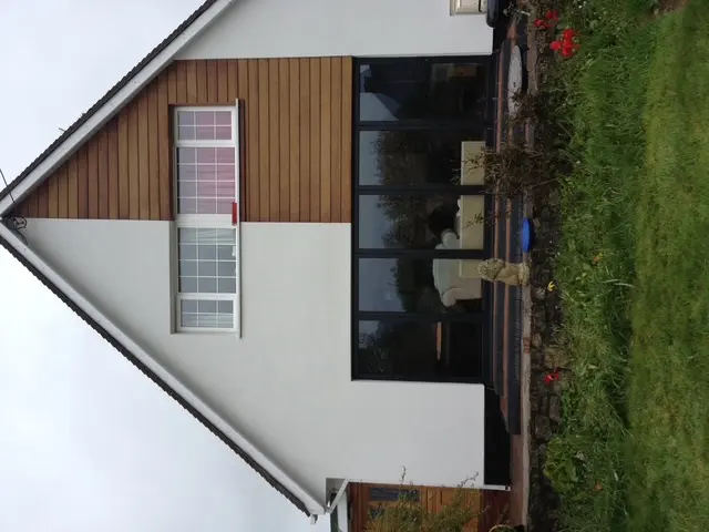 A modernised home exterior with crisp white rendering and timber cladding, demonstrating high-quality external wall insulation and rendering finishes.