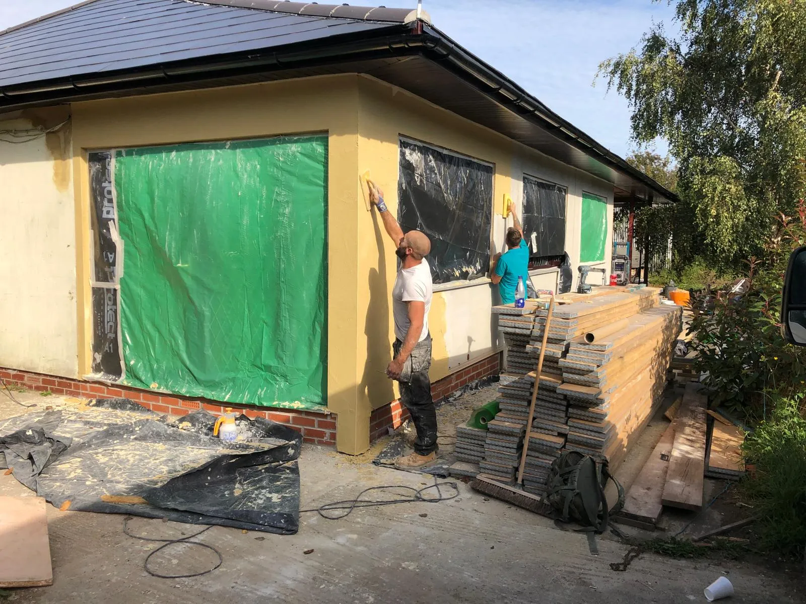 Builders applying yellow external render to the exterior walls of a house, showcasing professional external rendering services.