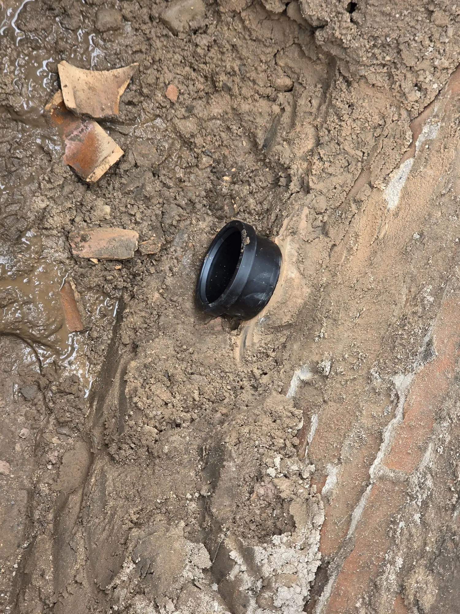 A picture of a new black drainage pipe exposed in a muddy trench