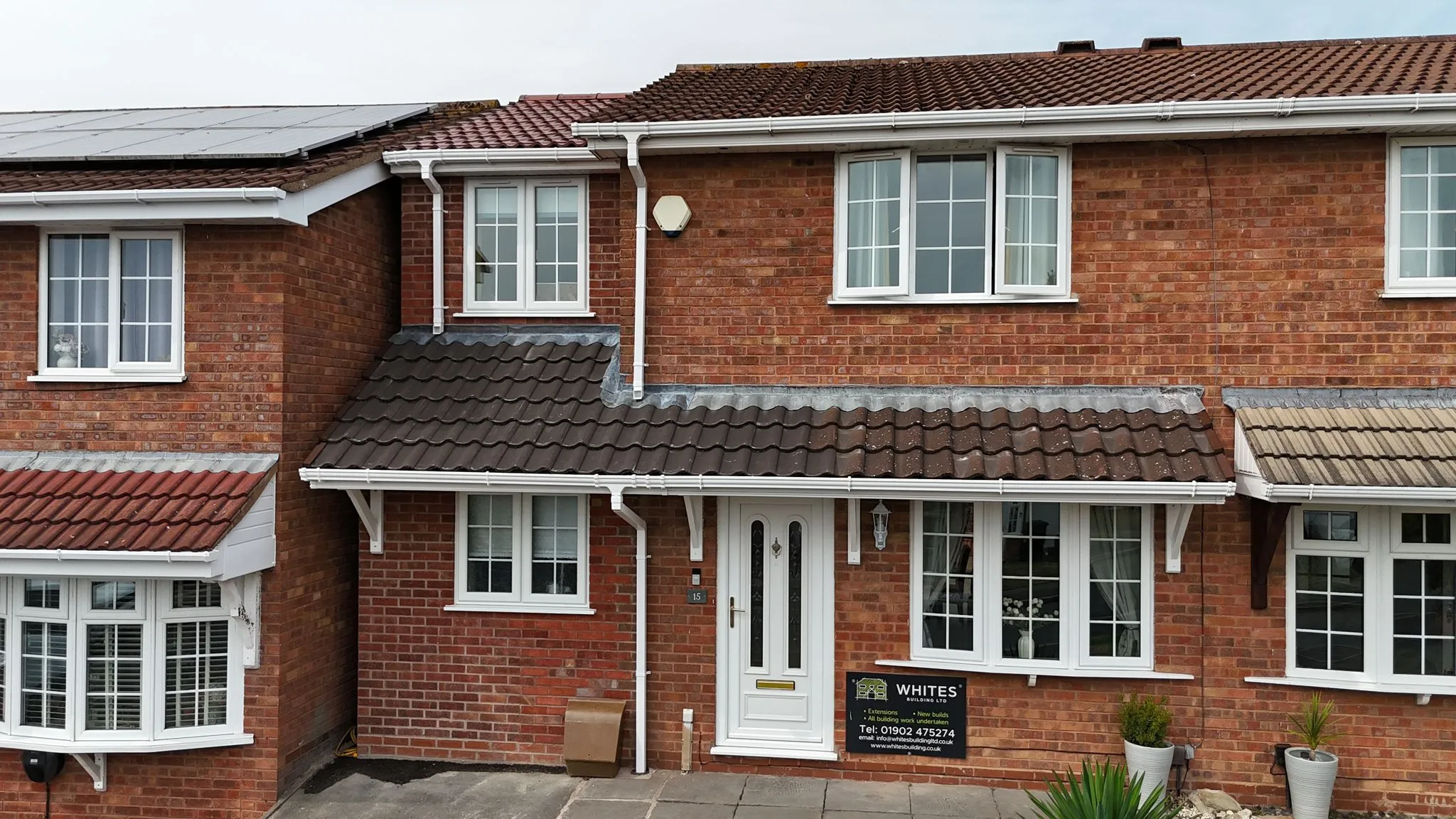 Front view of a red brick terraced house with white windows and a Whites Building LTD builder's sign.