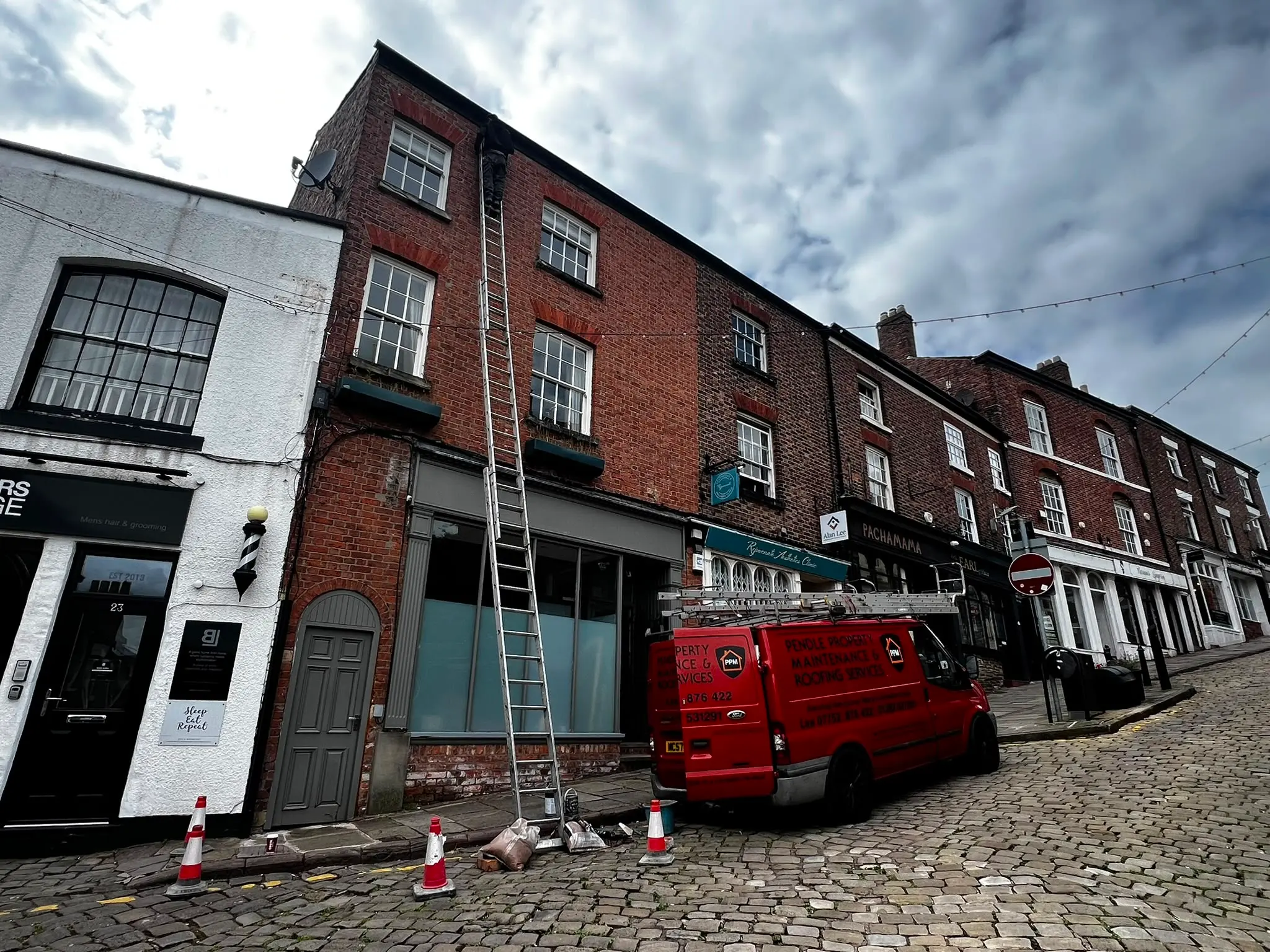 Pendle Property Maintenance roofer on a ladder outside a brick building