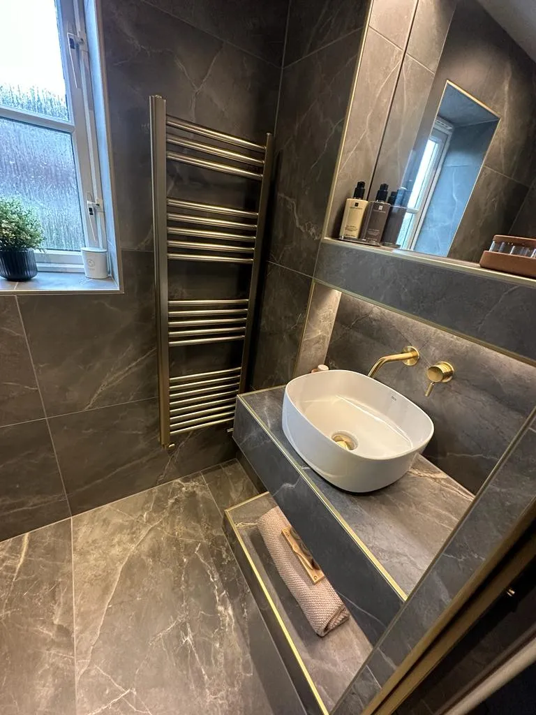 High-end luxury bathroom renovation in Plymouth featuring dark marble tiles and gold fixtures by Sands & Vossen.