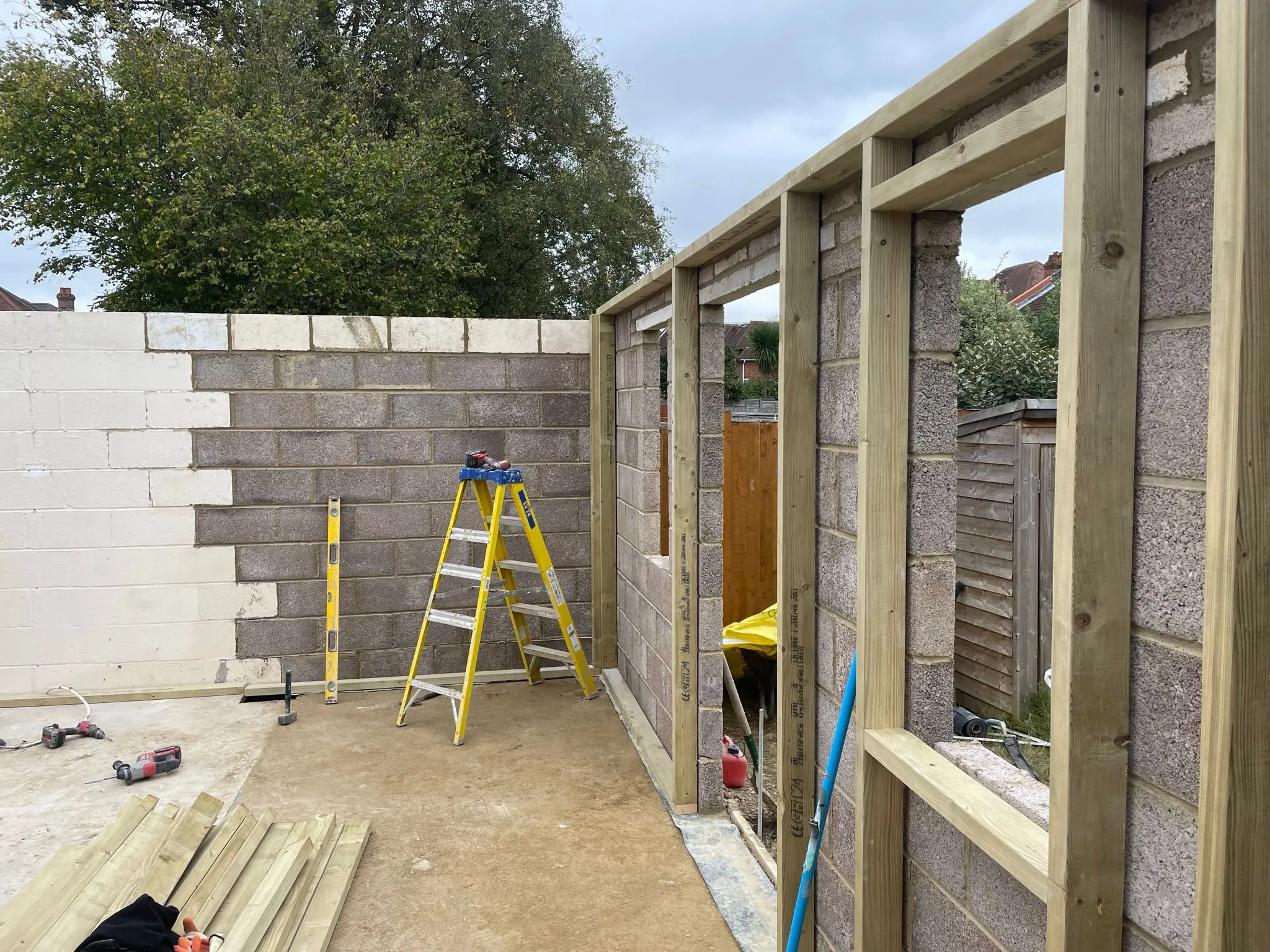 Structural timber framing and concrete blockwork being built for a single-storey house extension