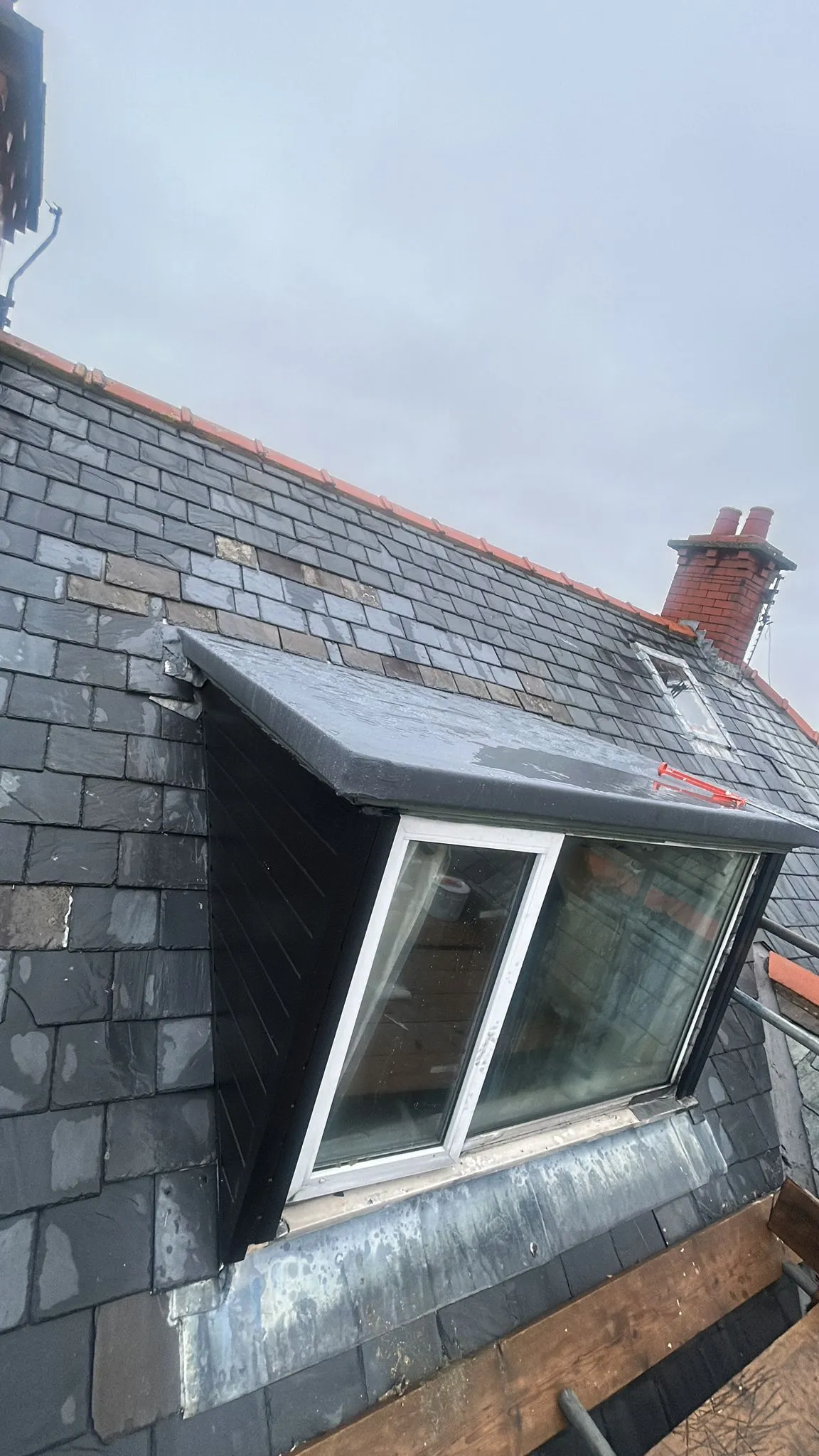 Slate roof with a dormer window and new lead flashing, featuring a chimney in the background and scaffolding, indicating ongoing roofing repairs or installation in Leicestershire.