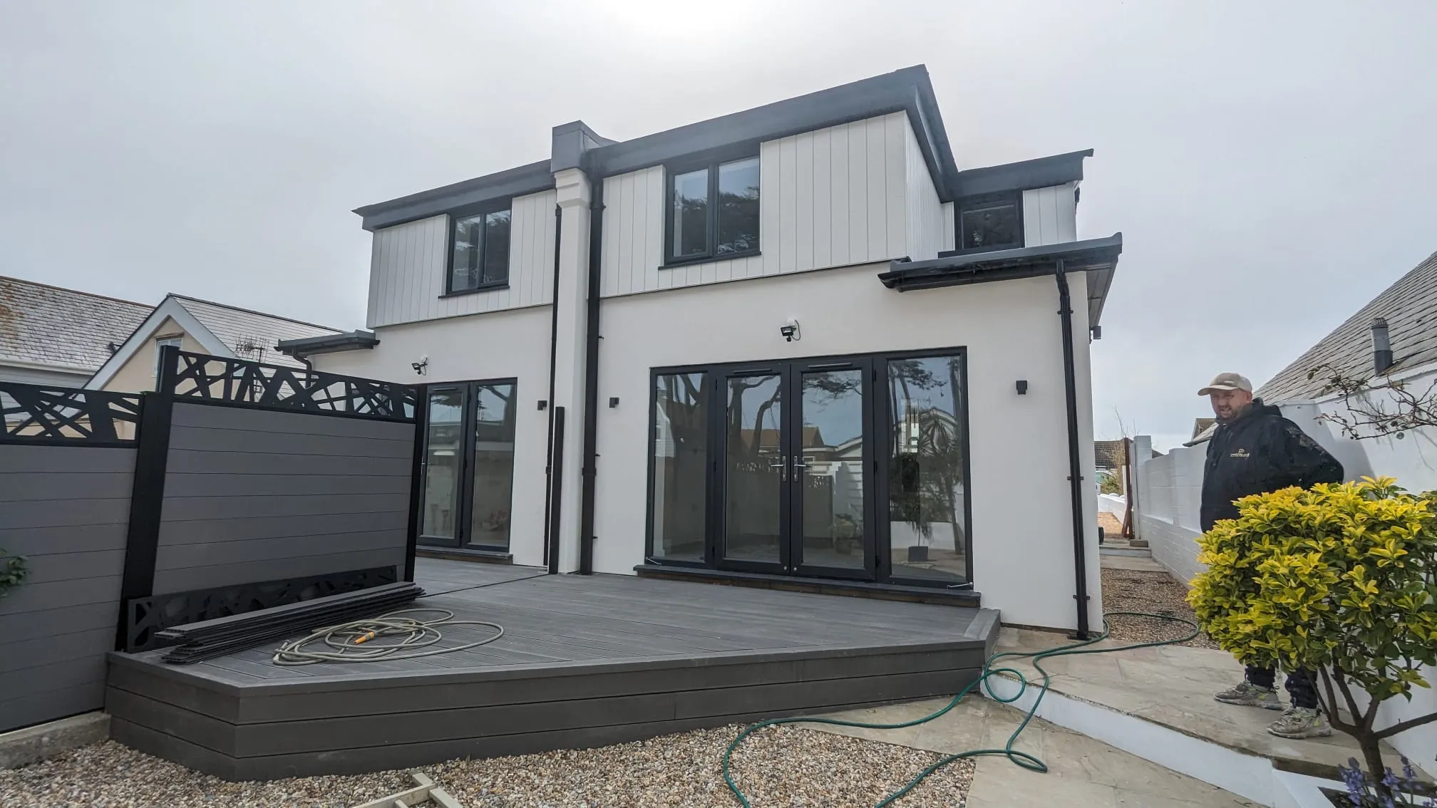 High-quality white external rendering on a modern house with black bifold doors and grey decking.