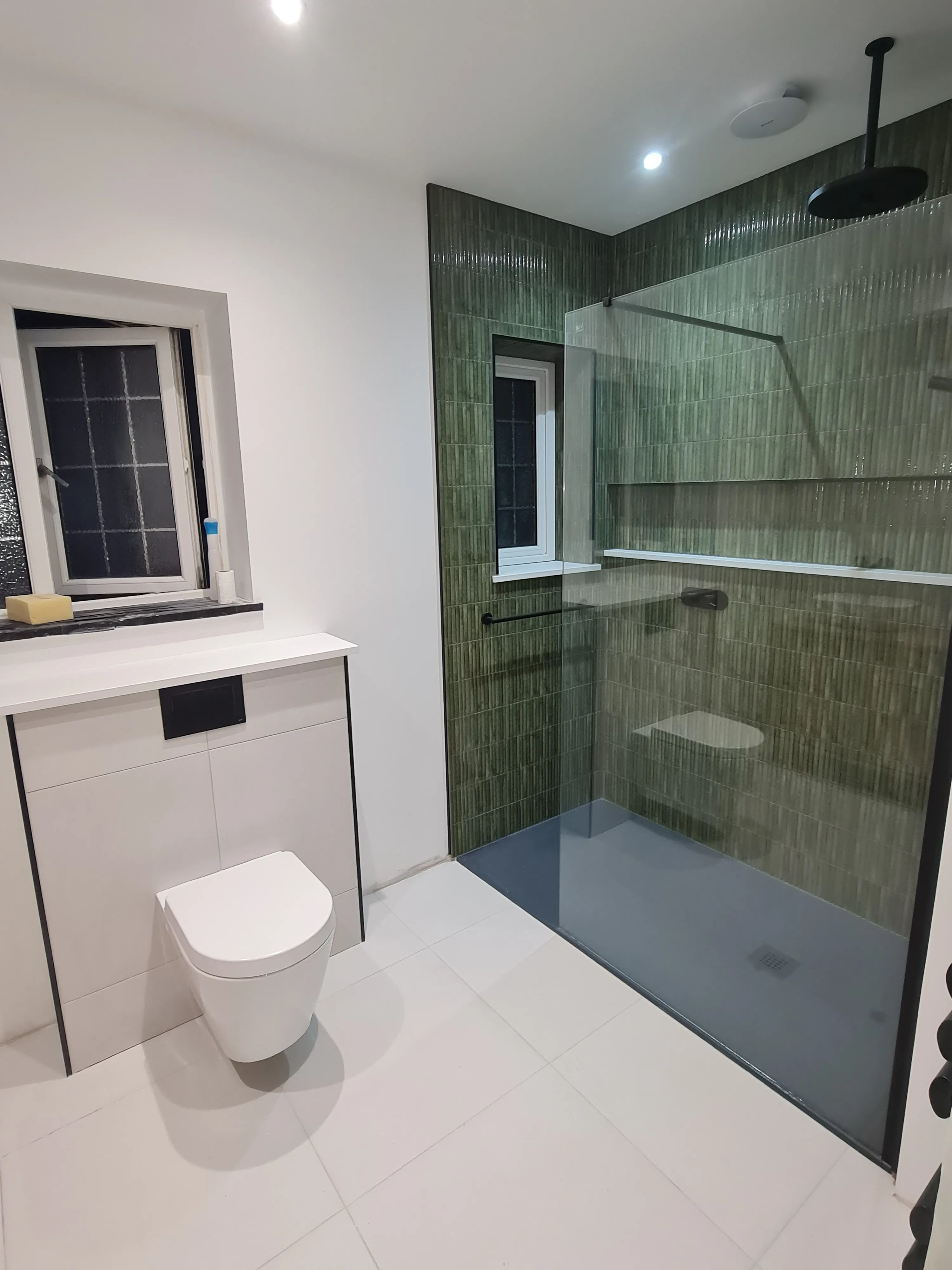 Luxury walk-in shower installation in Plymouth featuring green textured tiling and premium black fixtures by Sands & Vossen.