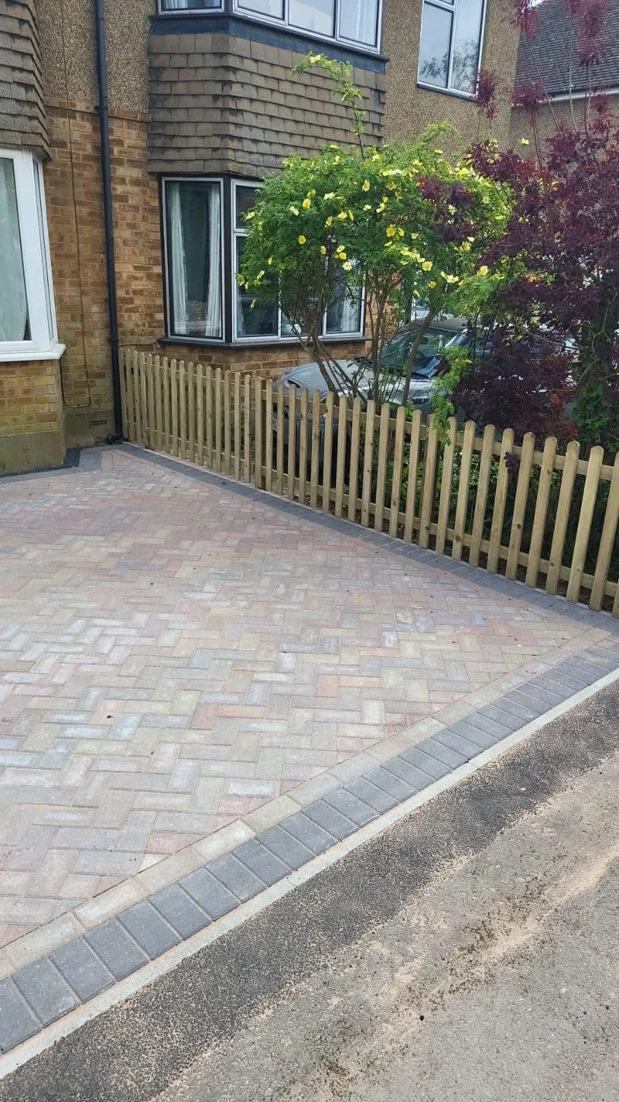 A professionally installed block paving driveway with a wooden picket fence in front of a residential property.