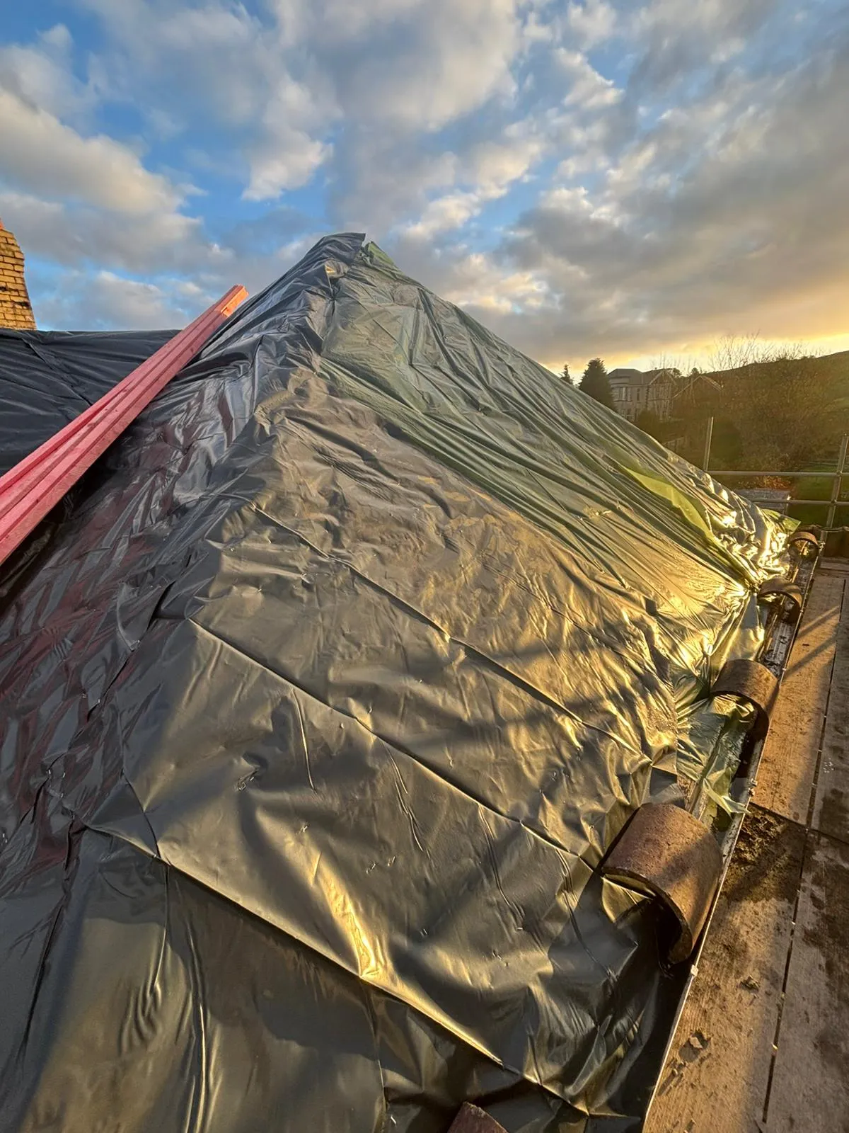 Emergency roof repair showing a pitched roof covered with a protective black plastic sheet in Gloucestershire