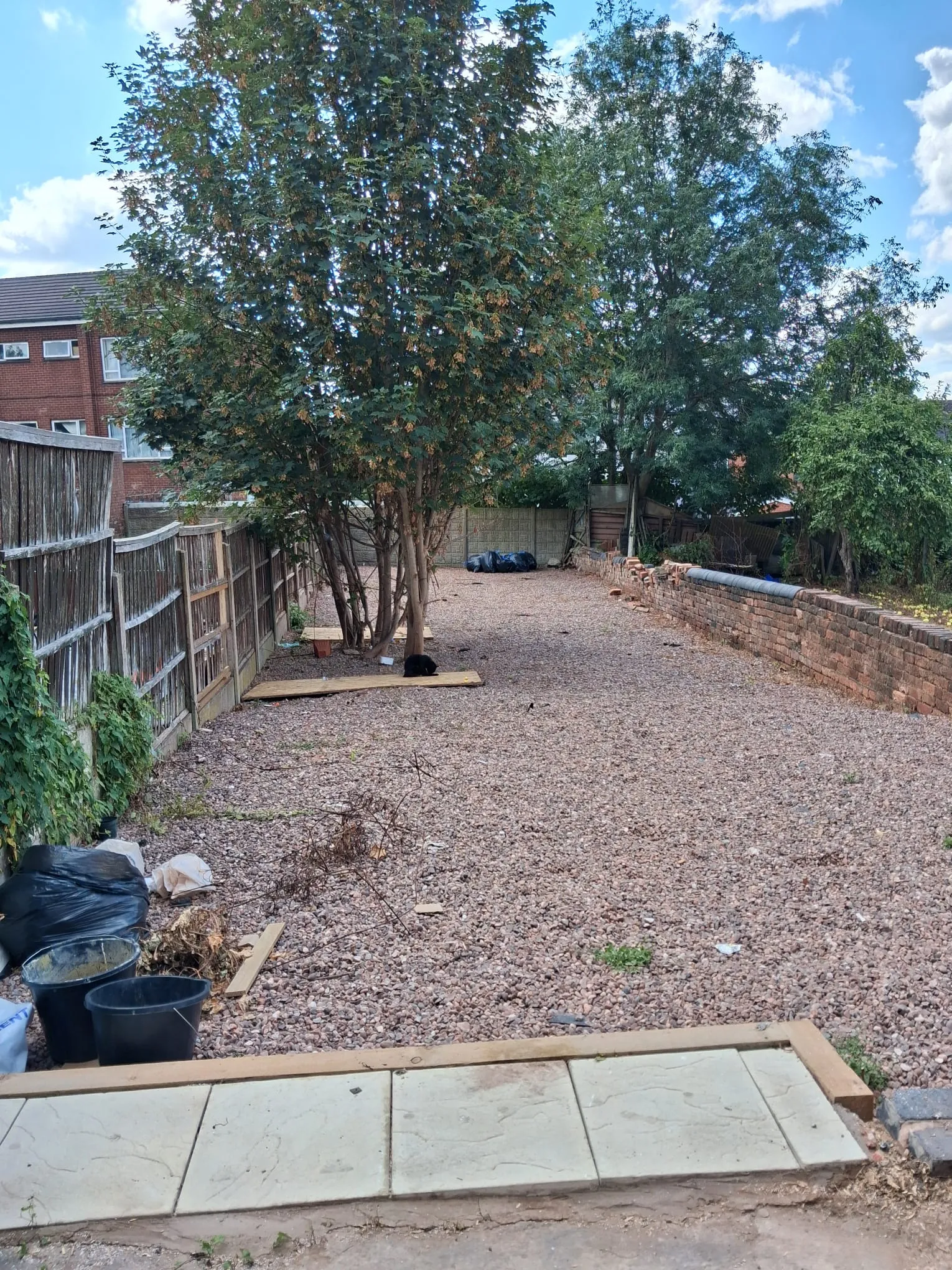 Cleared long residential garden with gravel surface, mature trees, and bagged garden waste ready for collection in Birmingham