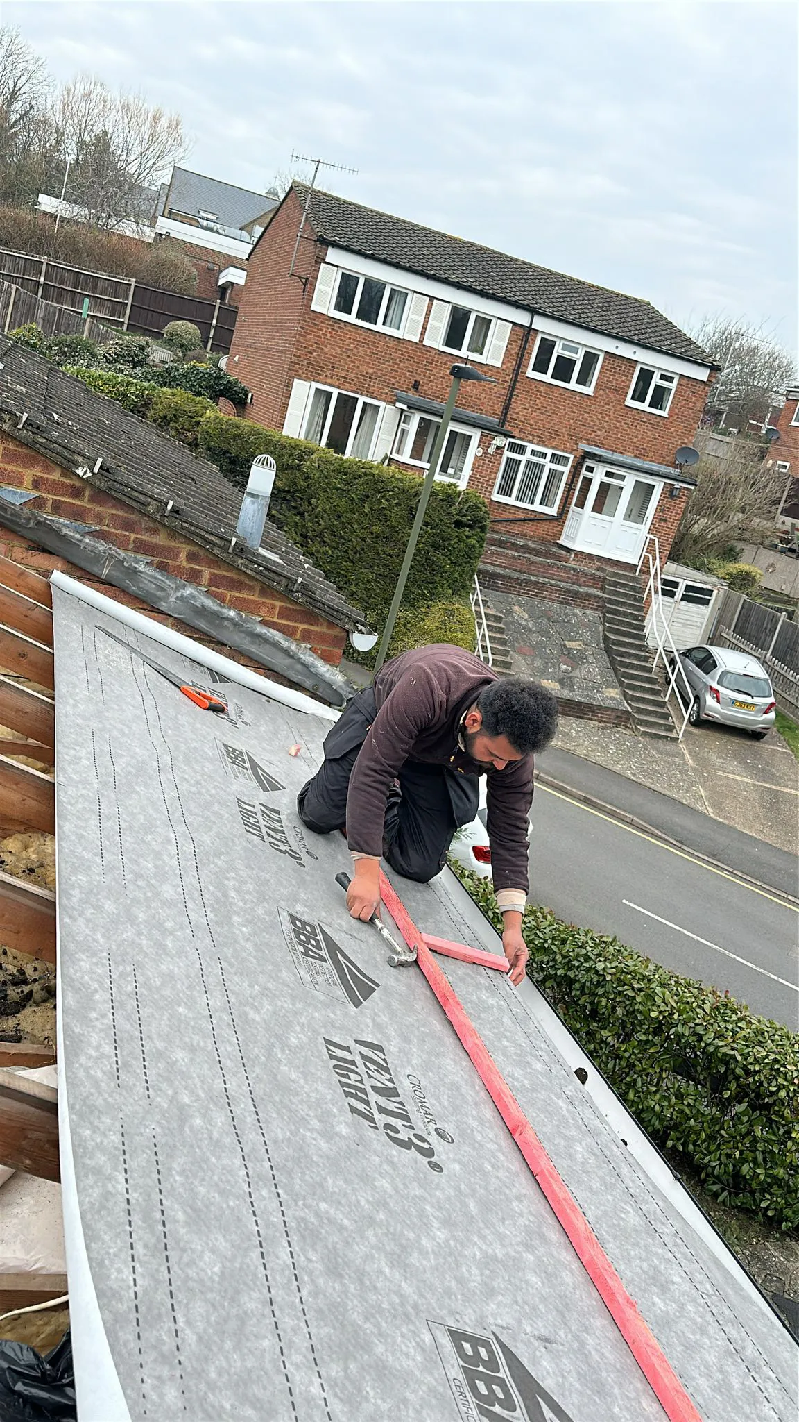 Roofer fixing treated roofing battens over breathable underlay on a pitched roof