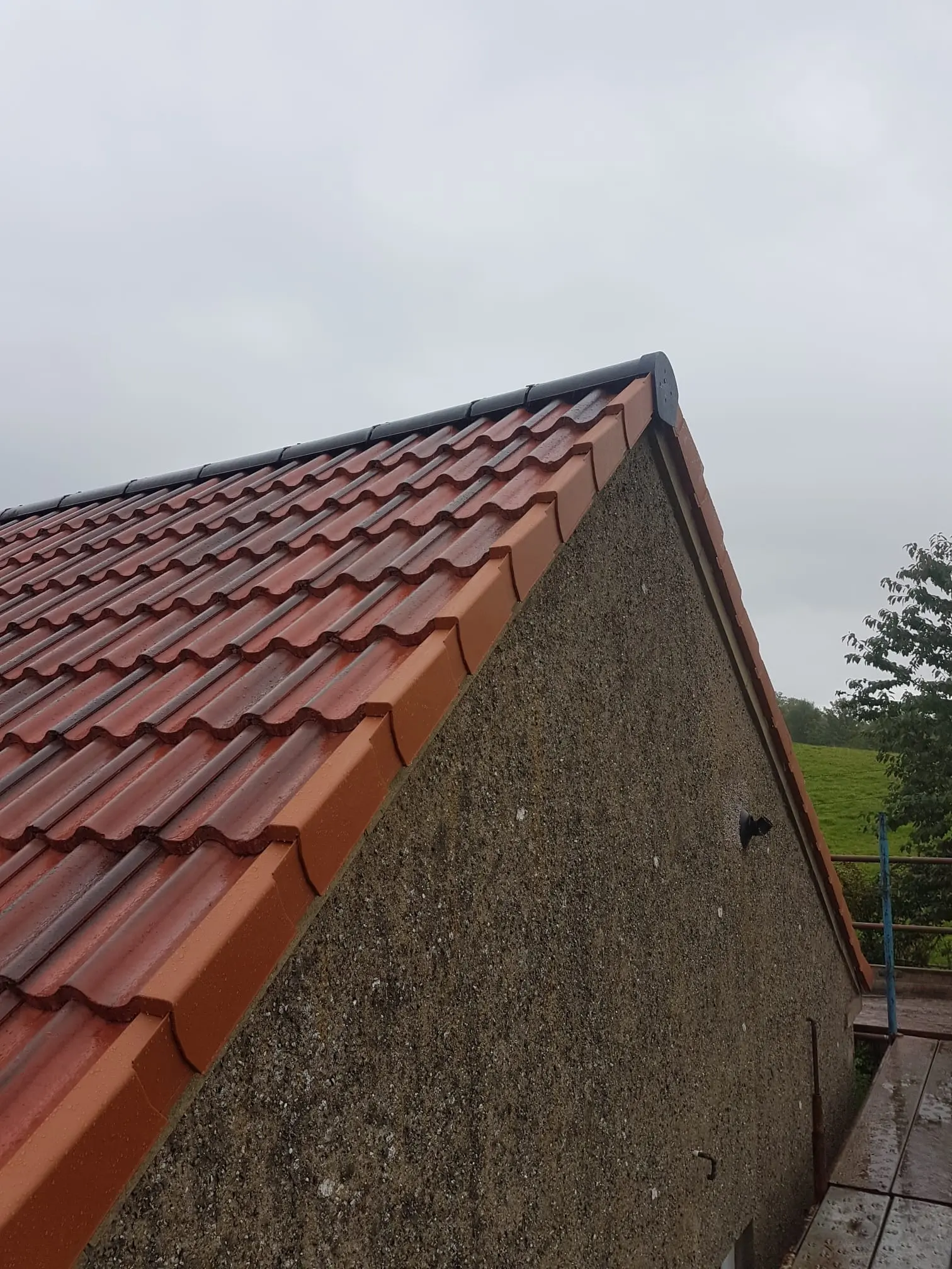 A newly installed red tiled roof with a dry verge edge and roughcast exterior wall.