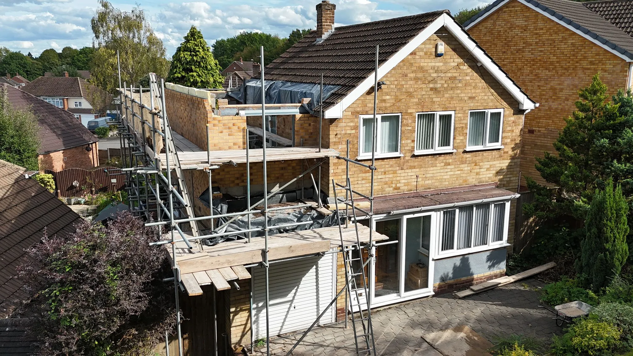An aerial view of a house extension project in progress, showing new two-storey brickwork and scaffolding on a residential property.