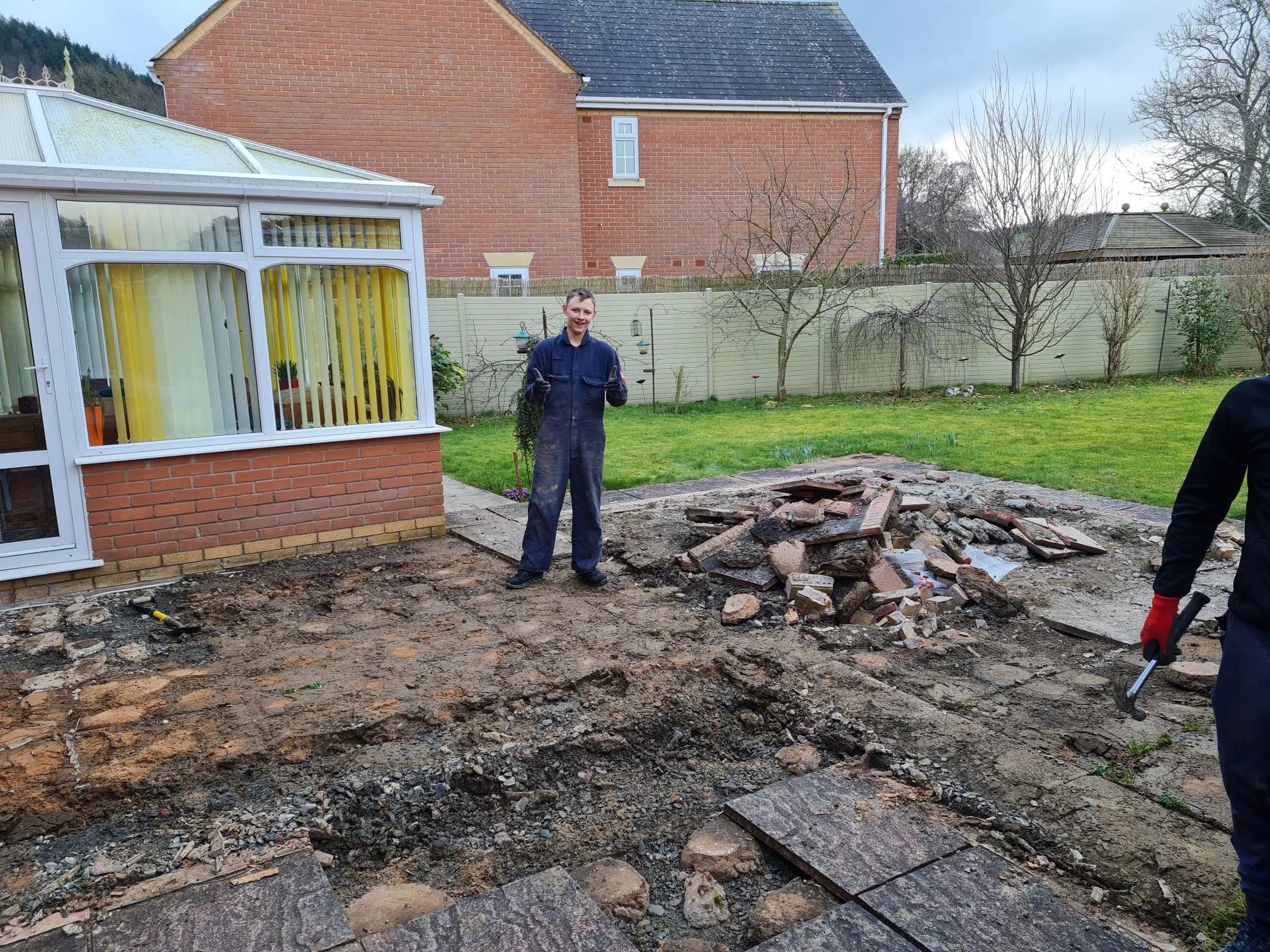A man in work clothes stands on a cleared area with rubble, signalling the initial phase of a new driveway or patio installation.