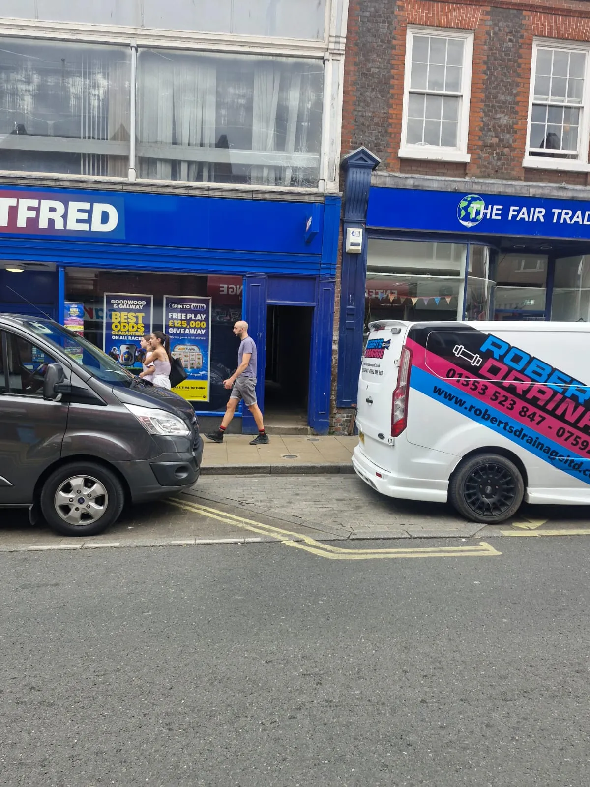 A white Roberts Drainage Ltd van parked on a street in Cambridgeshire near local shops.