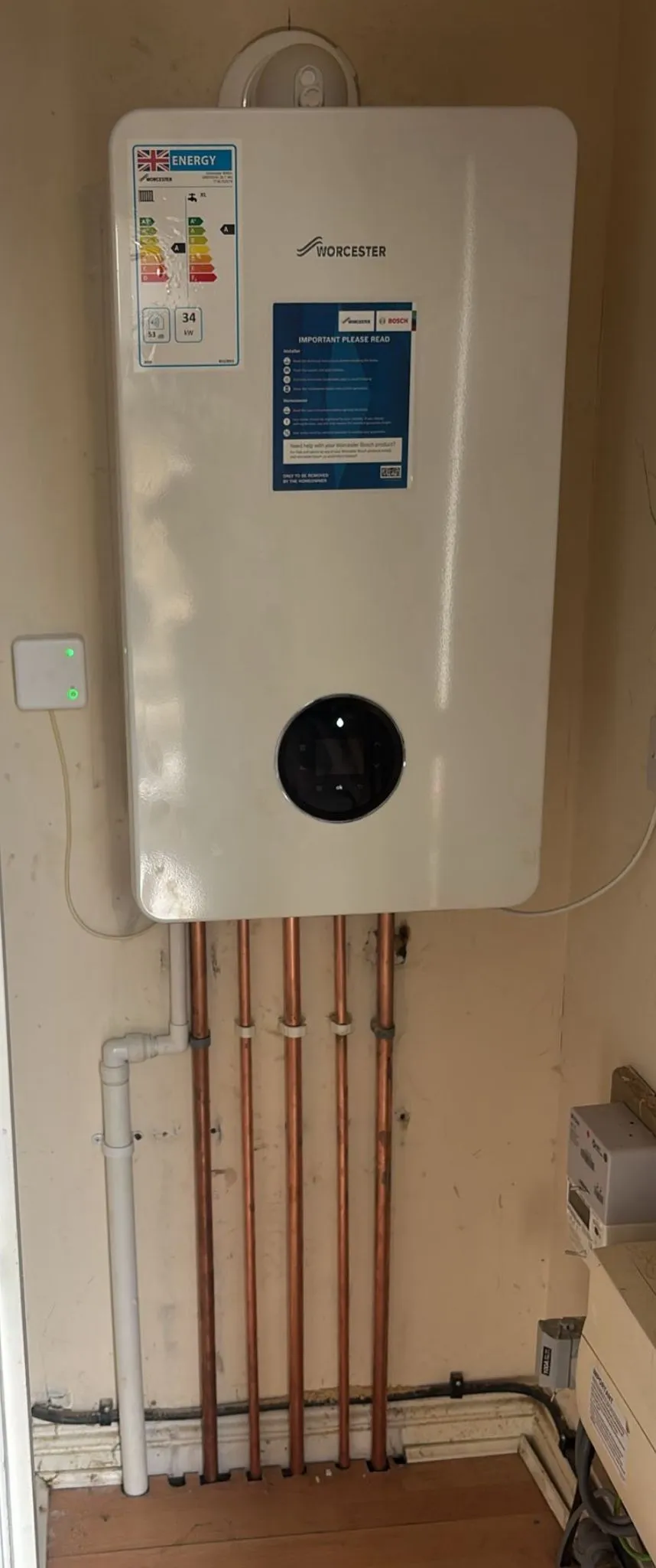 A modern Worcester Bosch combi boiler installed on a wall with copper pipes connected underneath.
