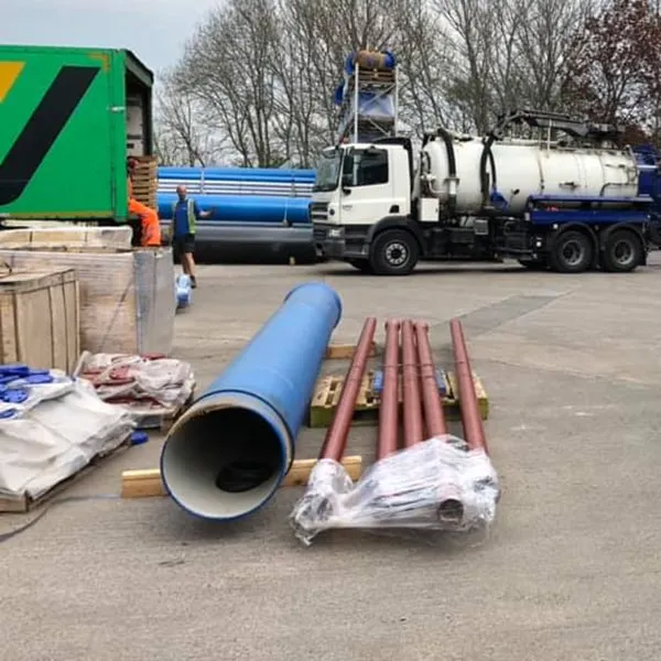 New blue and brown drainage pipes on a construction site with a tanker truck in the background, illustrating drain excavation and replacement.