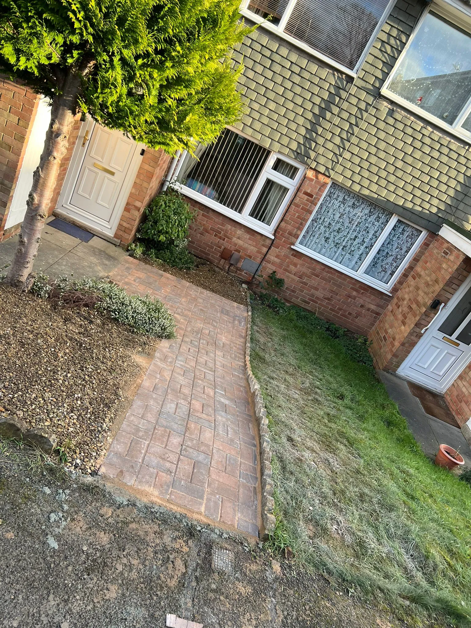 Front garden with a freshly laid block paved pathway, a gravel planting area, and a lawn, leading to a house entrance.