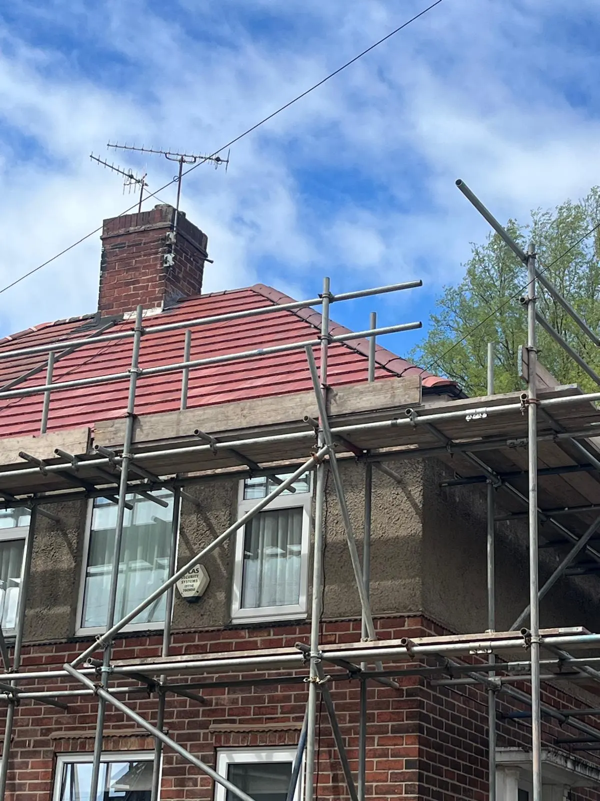 A newly installed red tile roof on a brick house surrounded by scaffolding during a roof replacement project