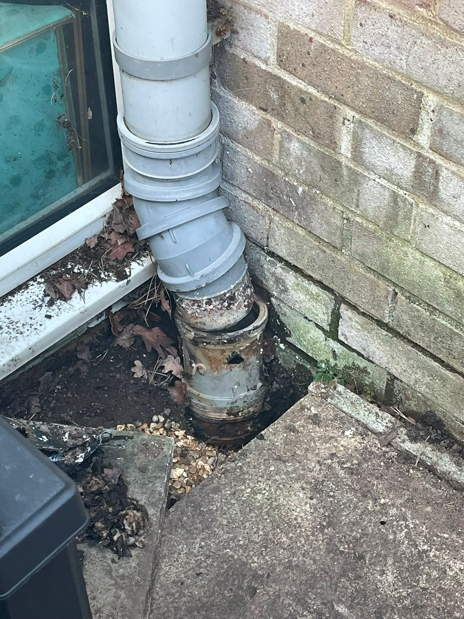 A broken exterior drain pipe disconnected from the ground drainage system near a brick wall