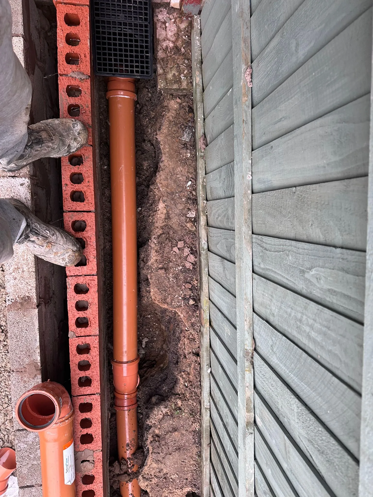 New orange drainage pipe being installed in a trench during a professional drain repair project in Macclesfield.