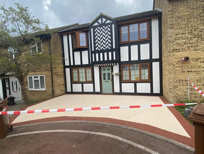 A modern two-tone resin-bound driveway in cream and red, freshly installed in front of a house with a distinctive black and white facade.