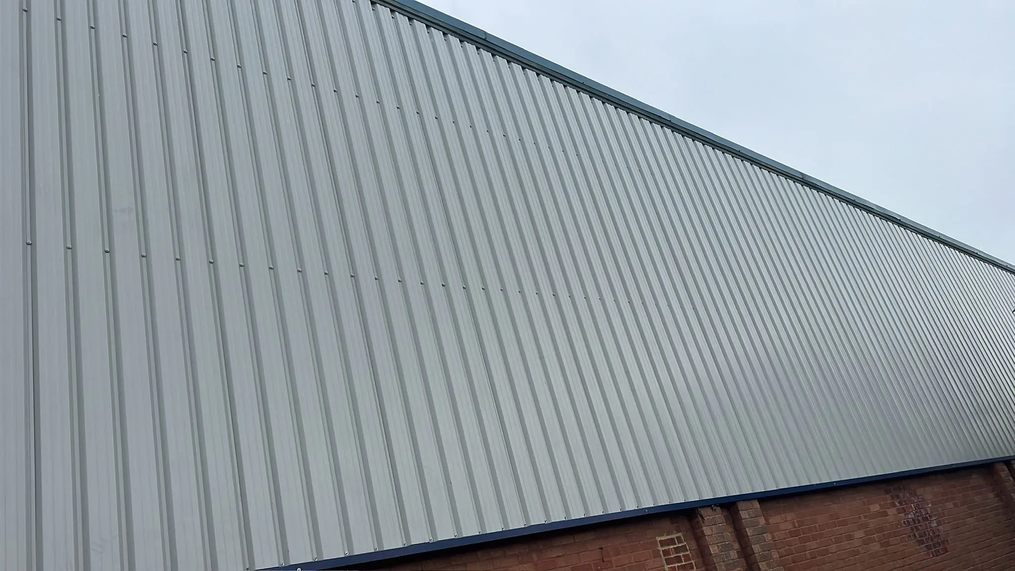 Exterior wall of an industrial building featuring weather-resistant corrugated metal cladding above a brick base.