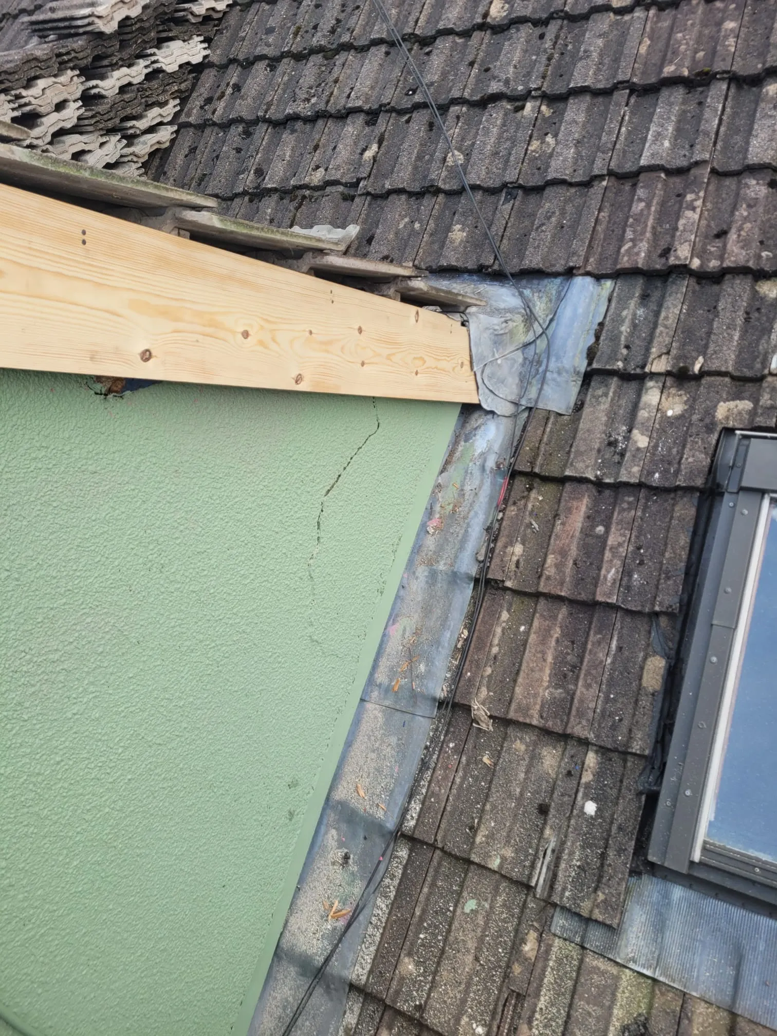 Roof repair in progress showing old roof tiles, new timber, cracked green render, and lead flashing around a dormer or skylight, highlighting the need for leadwork and roof maintenance.