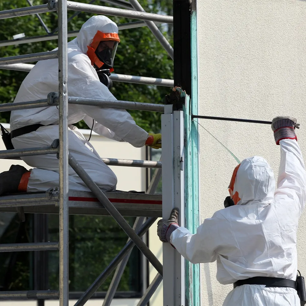 Stay Safe Environmental specialists in white hazmat suits and respirators removing asbestos panels from a property's exterior.