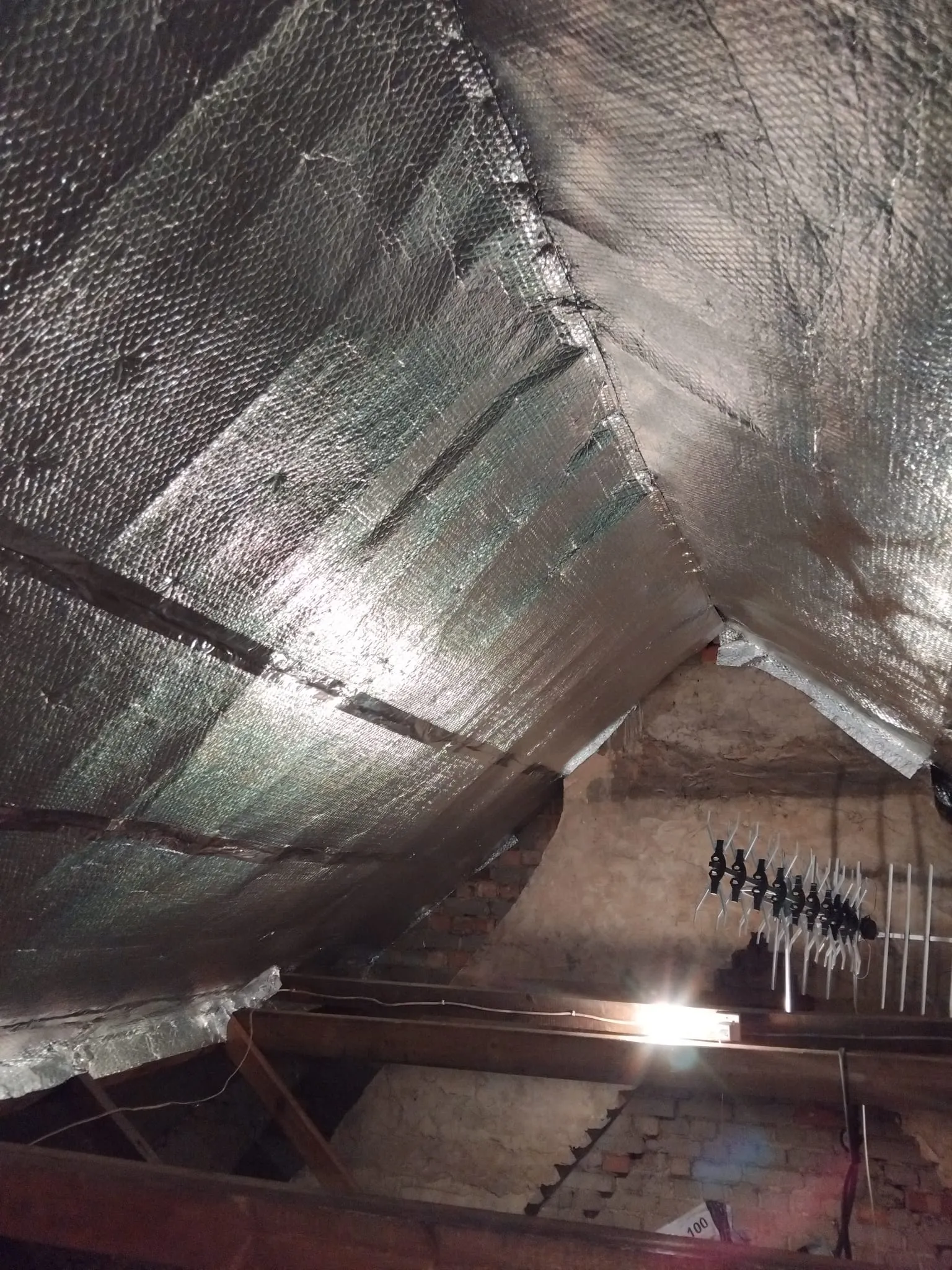 Loft space showing reflective foil insulation fitted along pitched roof rafters and ceiling joists