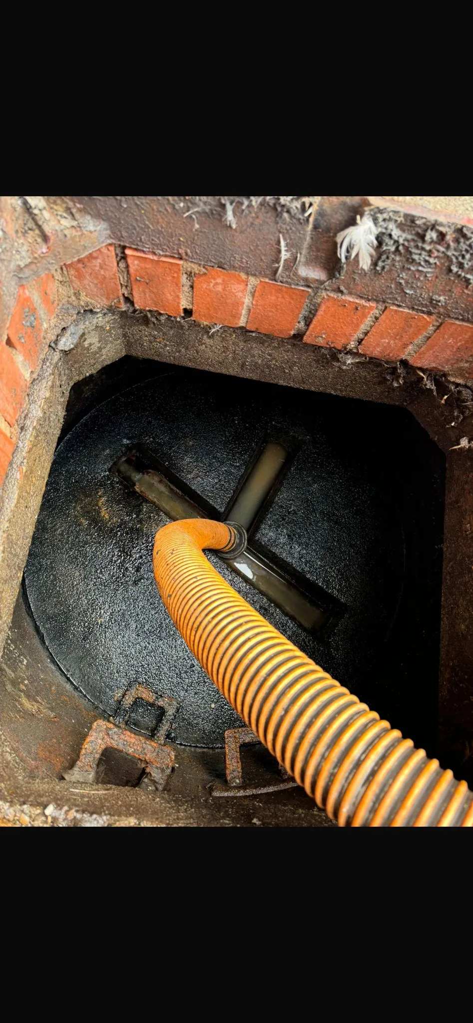 An orange hose inside a manhole, used for drain cleaning, septic tank emptying, or waste removal.