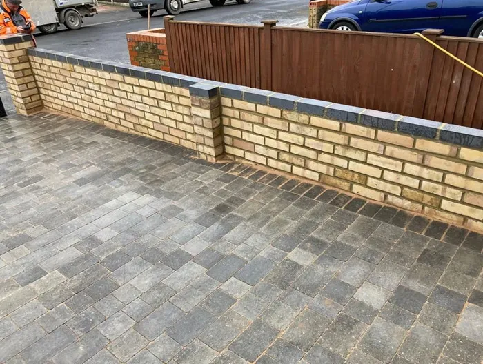 Newly laid block paving driveway in shades of grey, with an adjacent low brick garden wall topped with dark coping stones, enhancing the property's entrance.