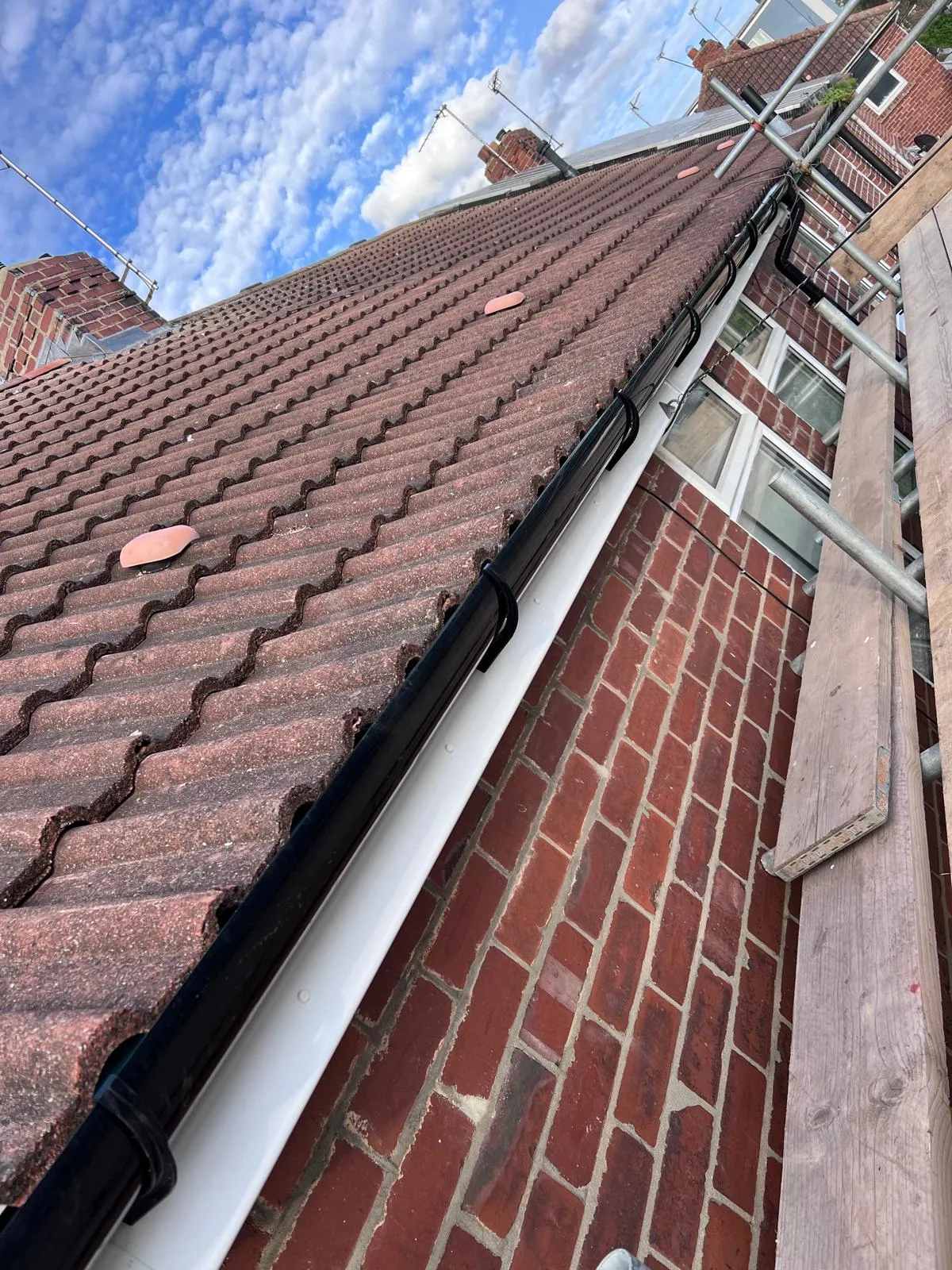 Close-up of a residential pitched tiled roof with newly installed black guttering, white fascia, and scaffolding.