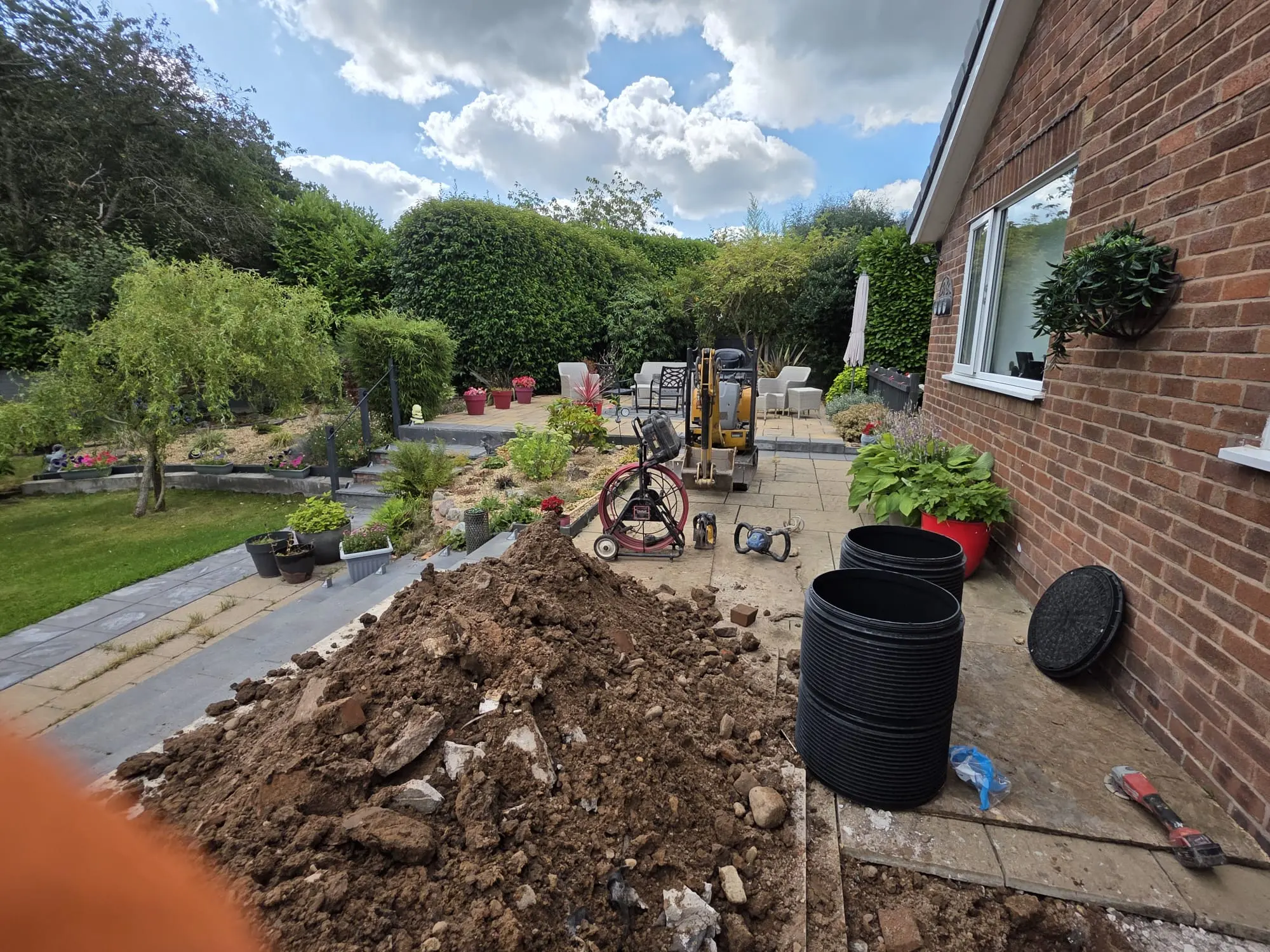 Excavated dirt pile and drainage inspection chambers on a patio during domestic drain replacement