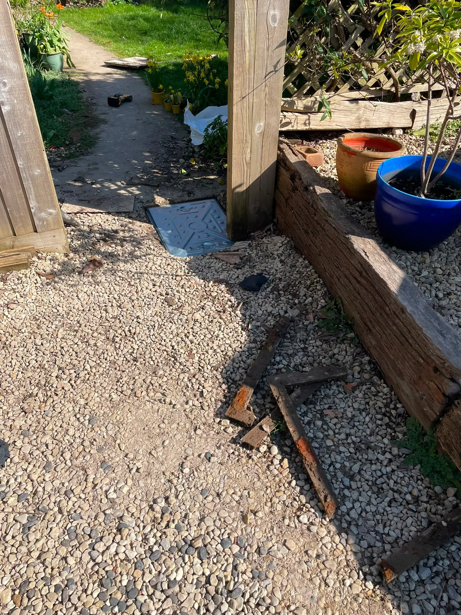 A newly installed metal manhole cover in a gravel garden path