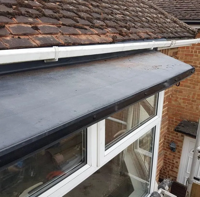 A professional flat roof installation on a residential property in Gloucestershire, featuring new guttering and a tiled roof.