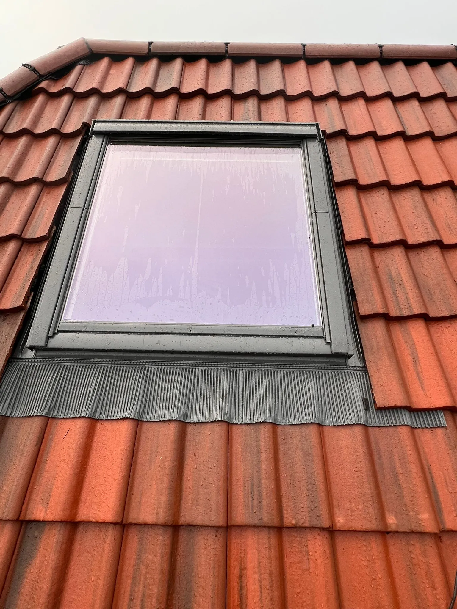 Velux roof window installed on a red tiled pitched roof with flashing.