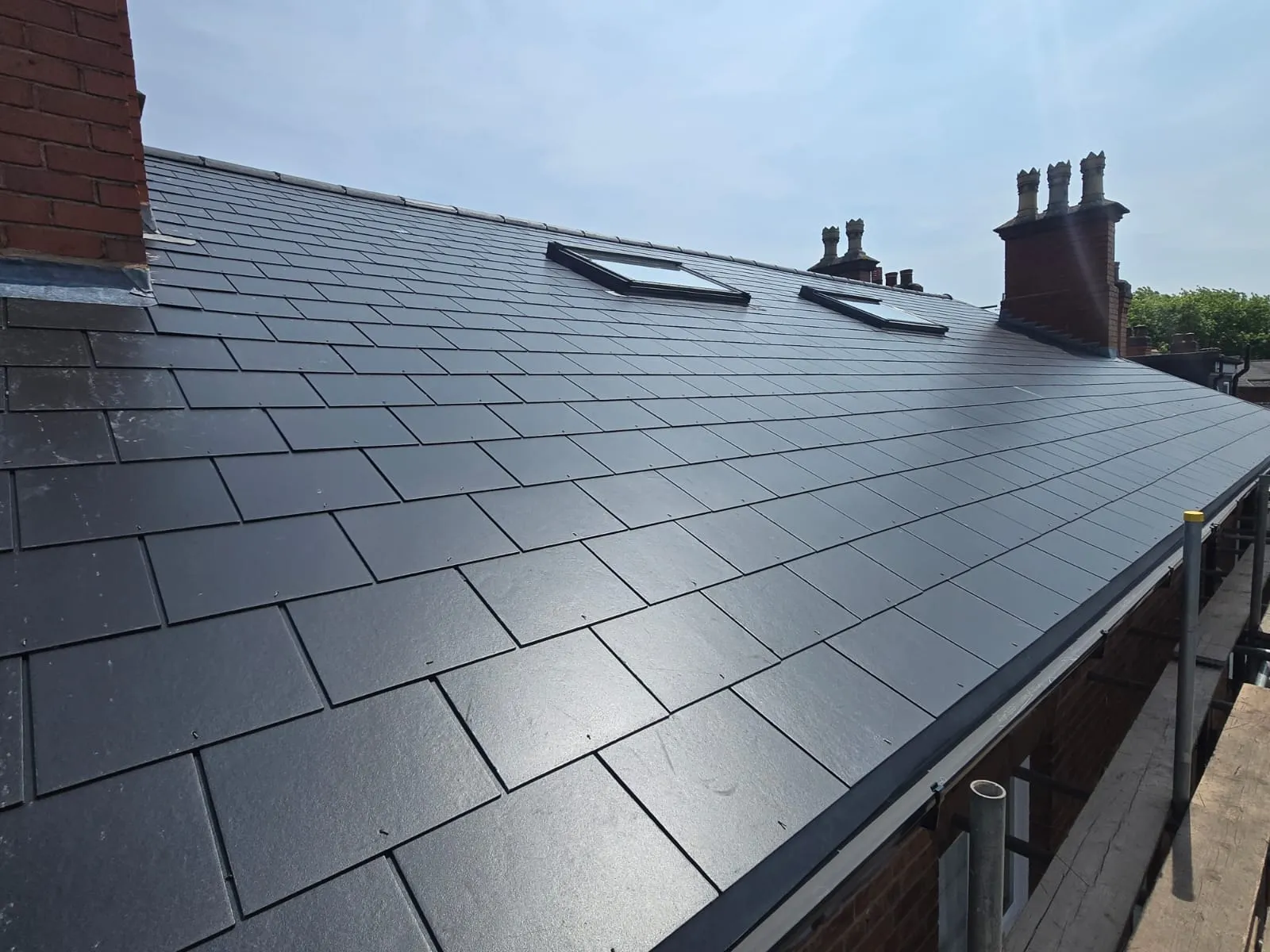 Newly installed dark grey slate roof with two skylights and brick chimneys on a property in Birmingham or Worcestershire.
