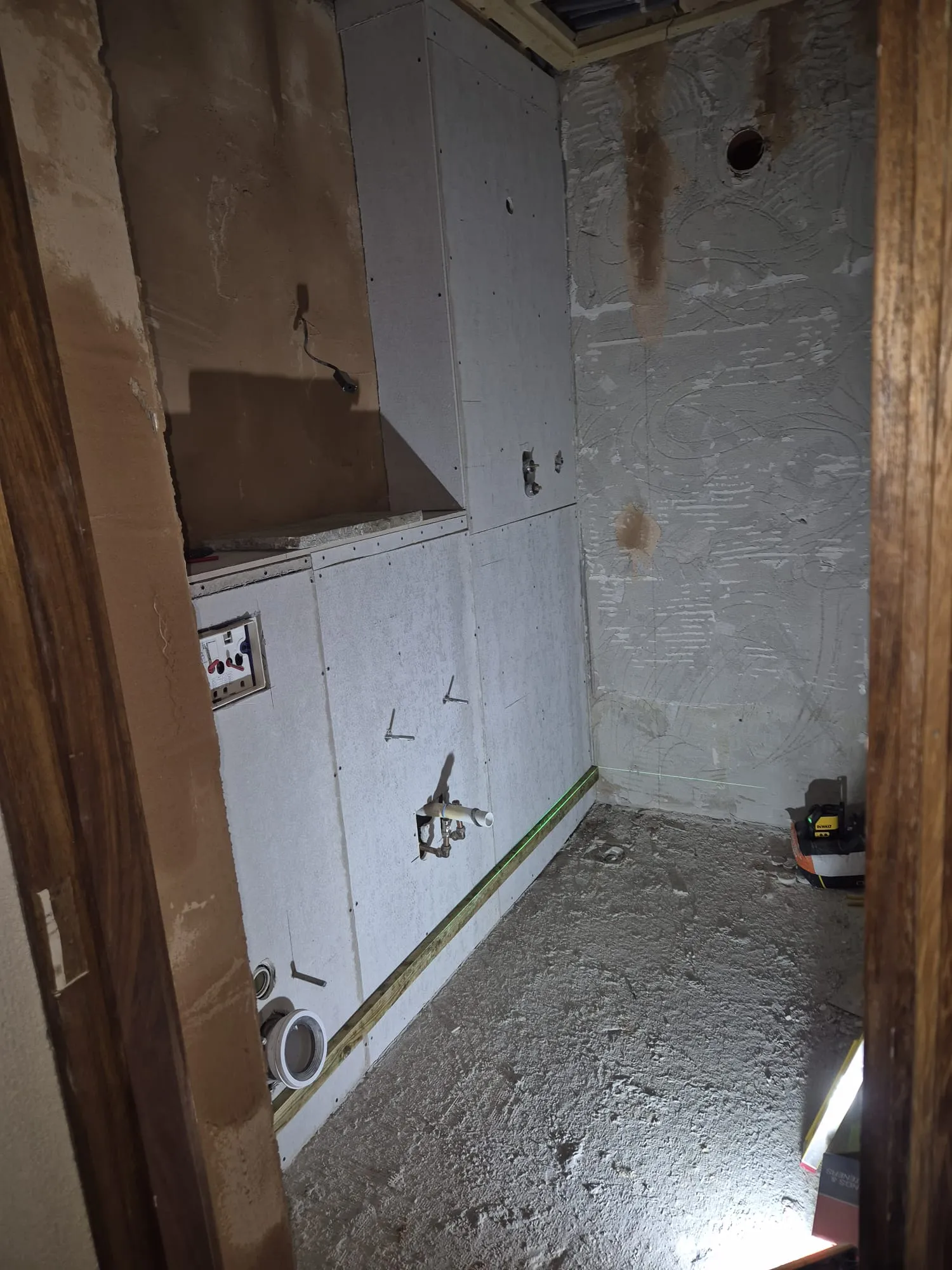 Room interior under renovation with plasterboard walls, exposed pipes, and electrical wiring, ready for tiling or decoration.