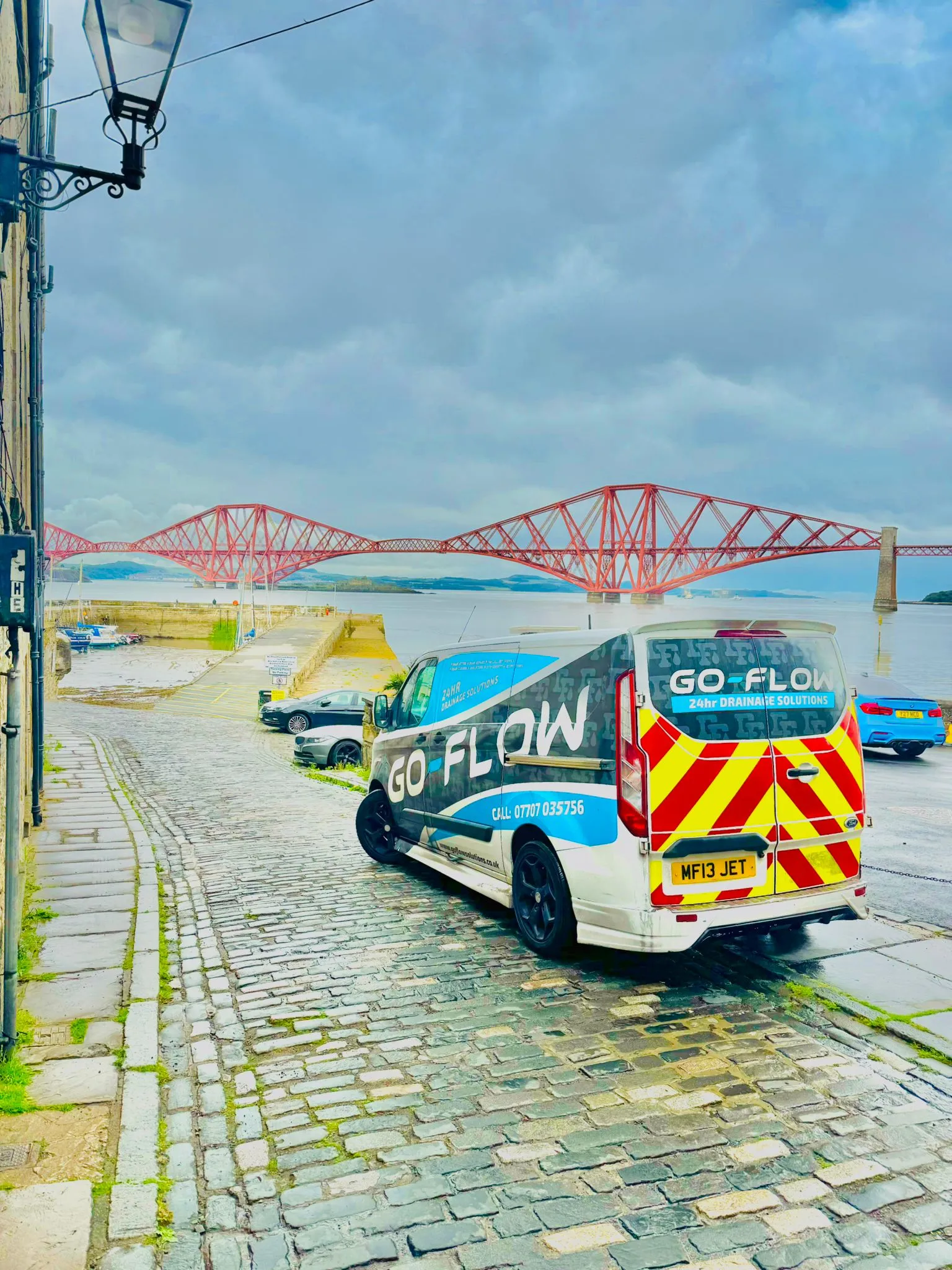 Go Flow Solutions branded drainage van on a cobbled street in Queensferry, Edinburgh, with the Forth Bridge in the background.