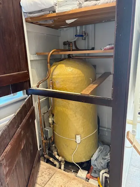 An insulated hot water tank inside an airing cupboard with copper pipes