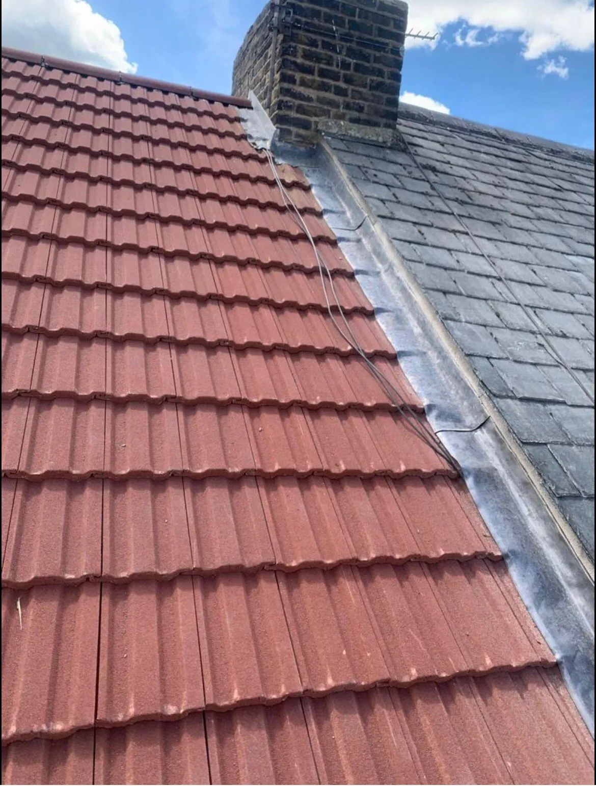 Tiled roof installation with lead flashing abutment next to a slate roof and brick chimney