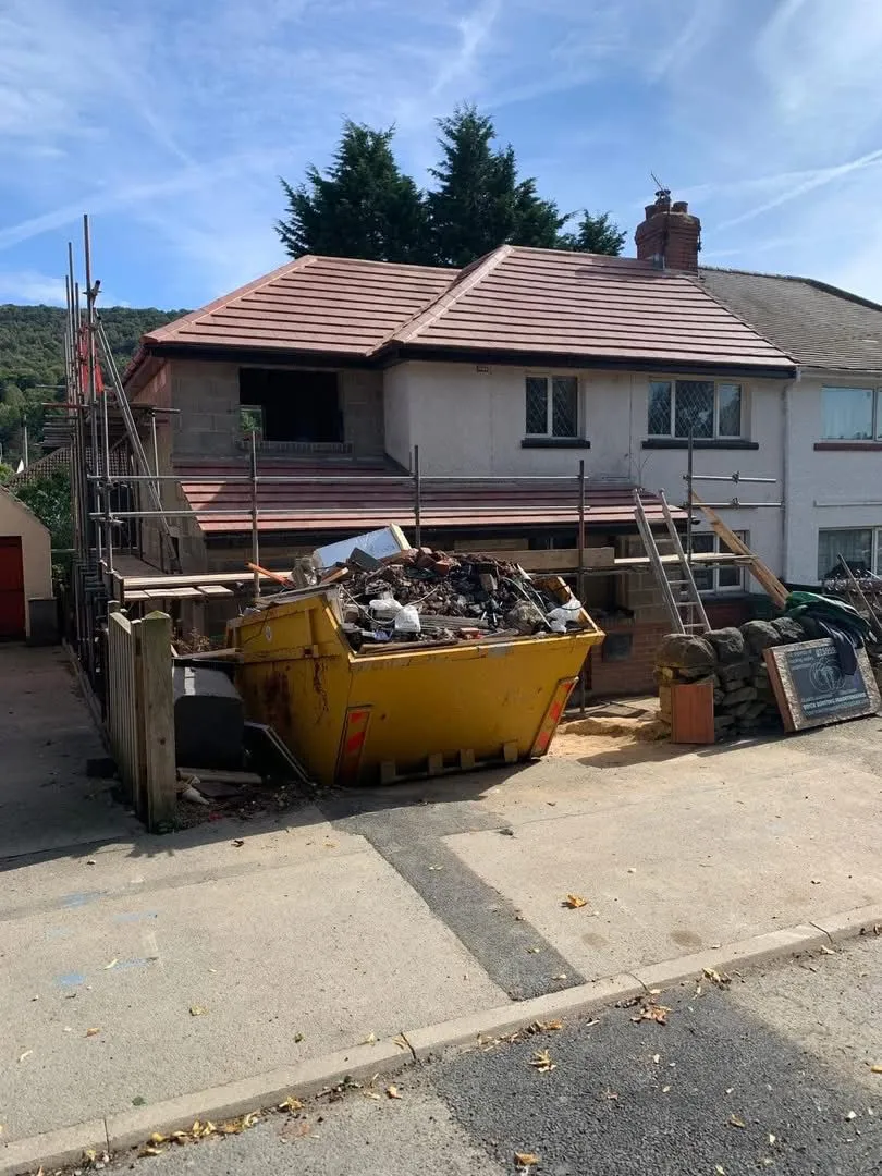A house with a newly installed tiled roof, scaffolding, and a full yellow skip during a professional re-roofing project.