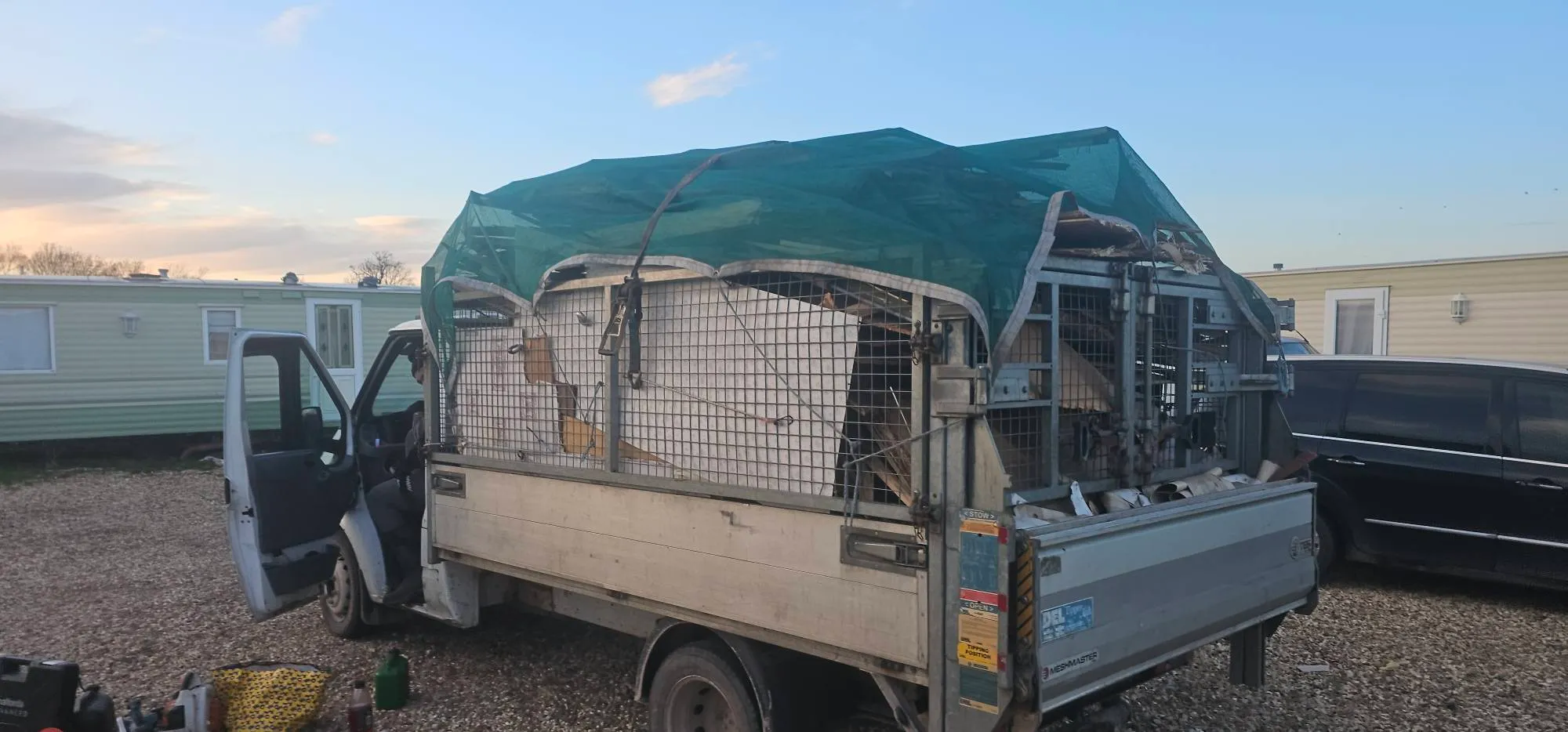 A caged waste removal truck loaded with timber and clearance debris secured under green netting