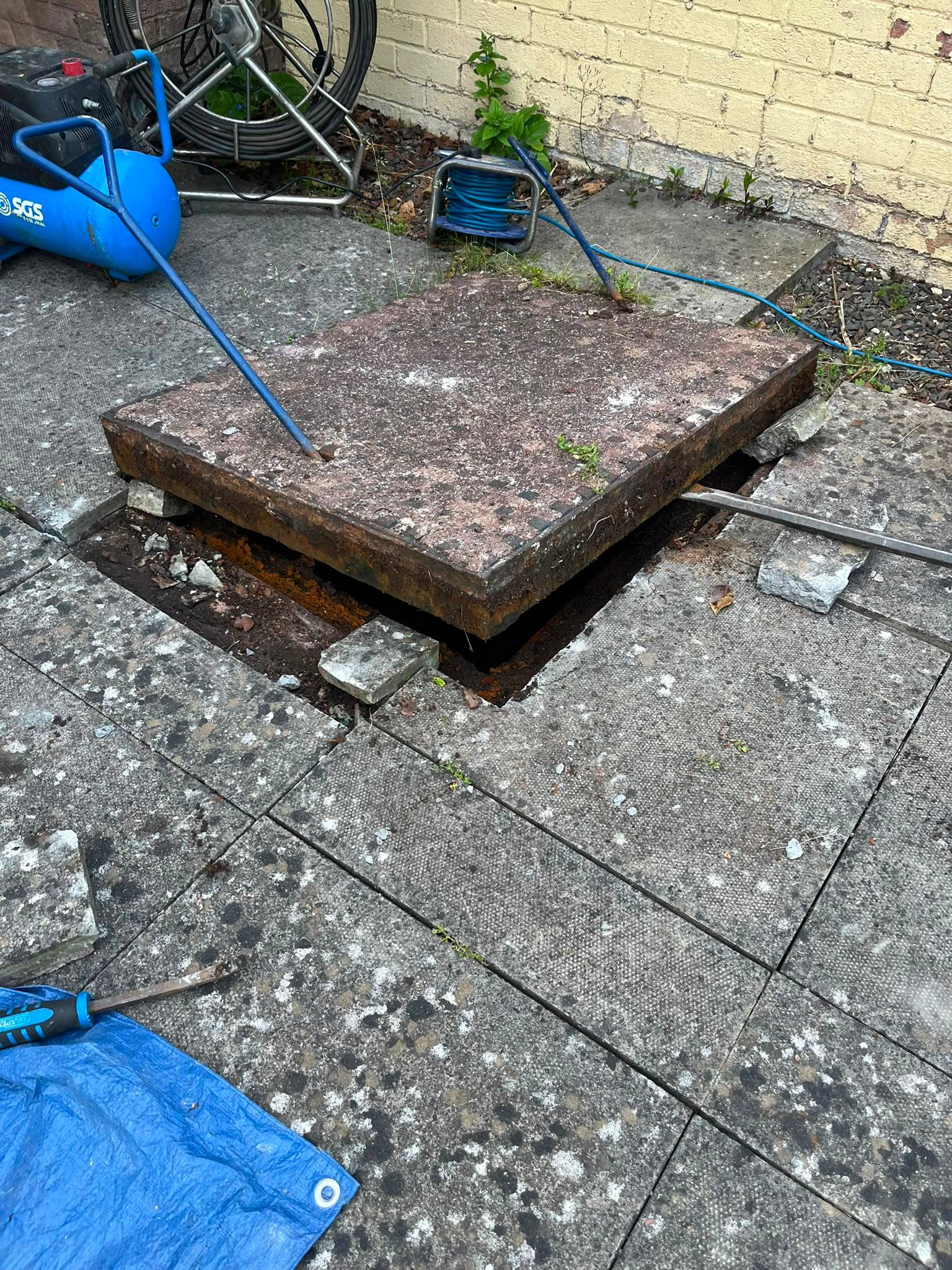CB Drainage professional lifting a heavy manhole cover to access the underground drainage system for inspection and clearance in Alloa, Clackmannanshire