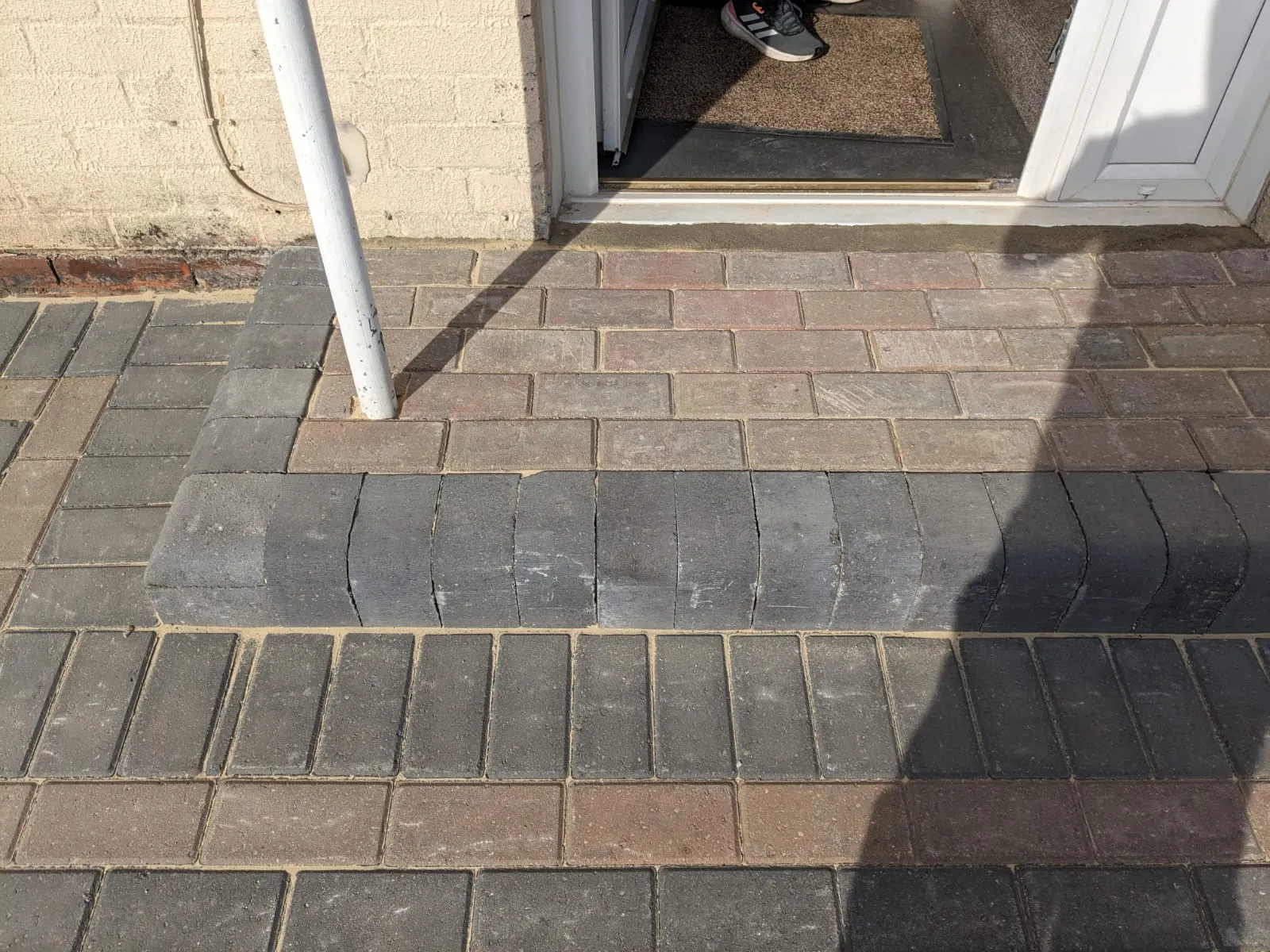 Close-up of a freshly laid block paved pathway and step in front of a house entrance, showcasing a two-tone pattern of grey and reddish-brown pavers.
