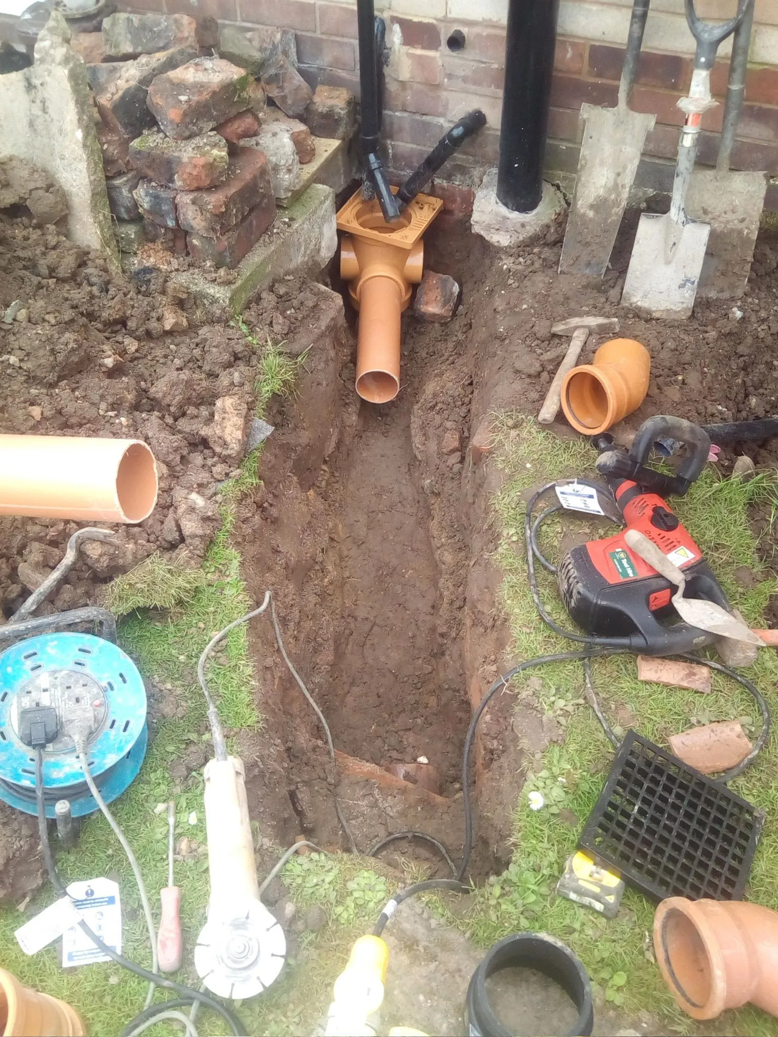 Drainage repair excavation showing new orange pipes and groundworks tools in Macclesfield