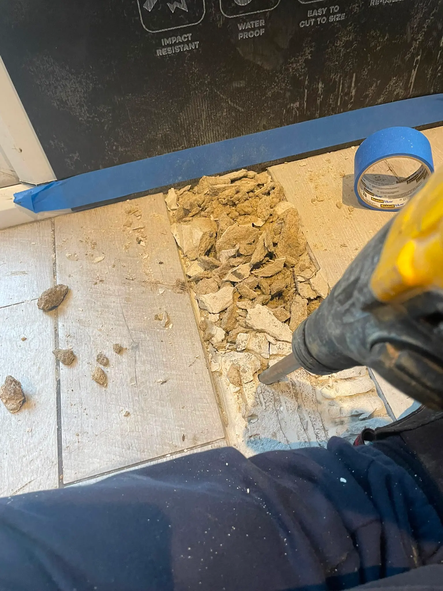 Plumber using a breaker tool to excavate a tiled floor for drainage or plumbing repairs