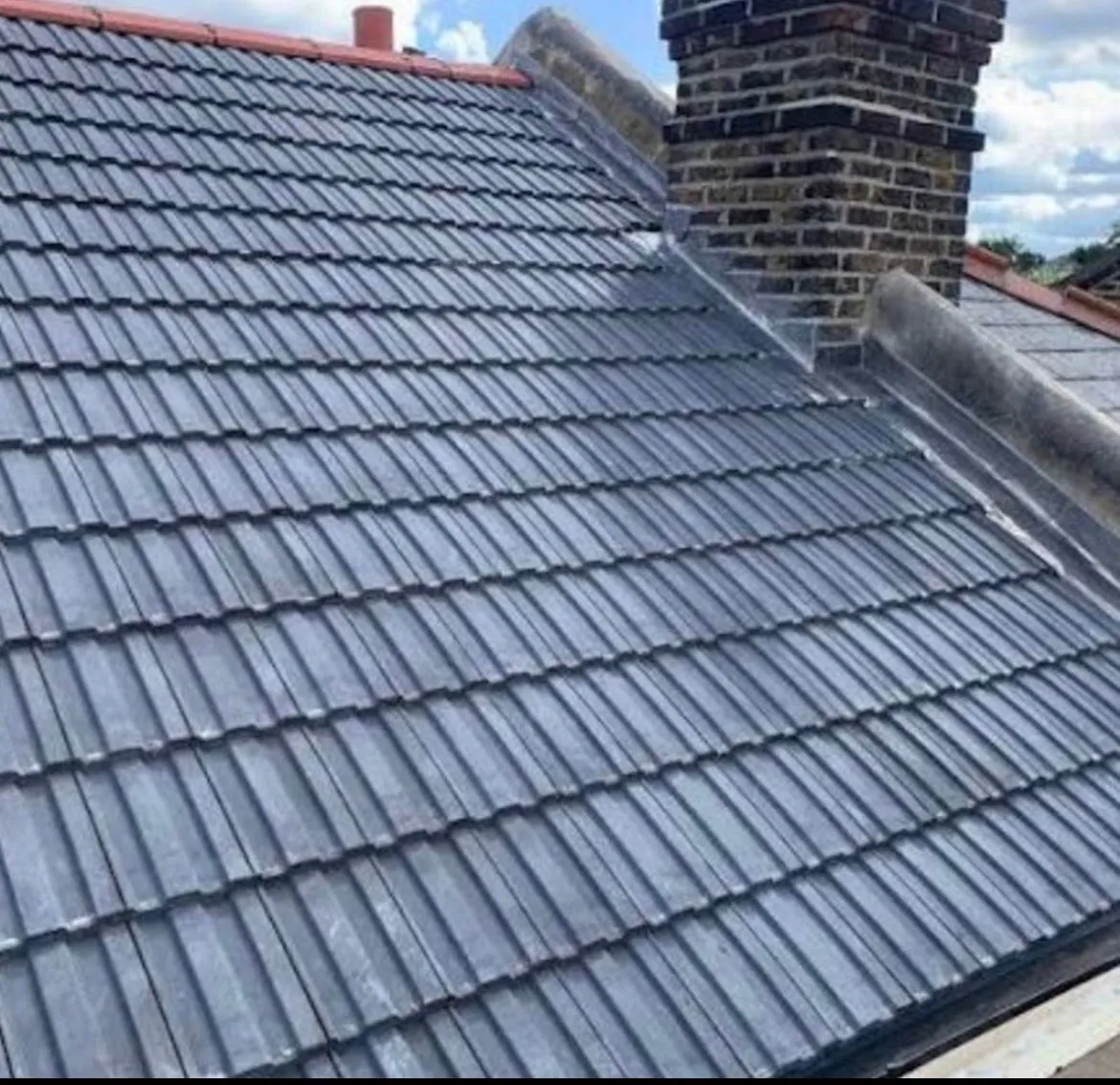 Completed pitched tiled roof installation with fresh lead flashing alongside a brick chimney
