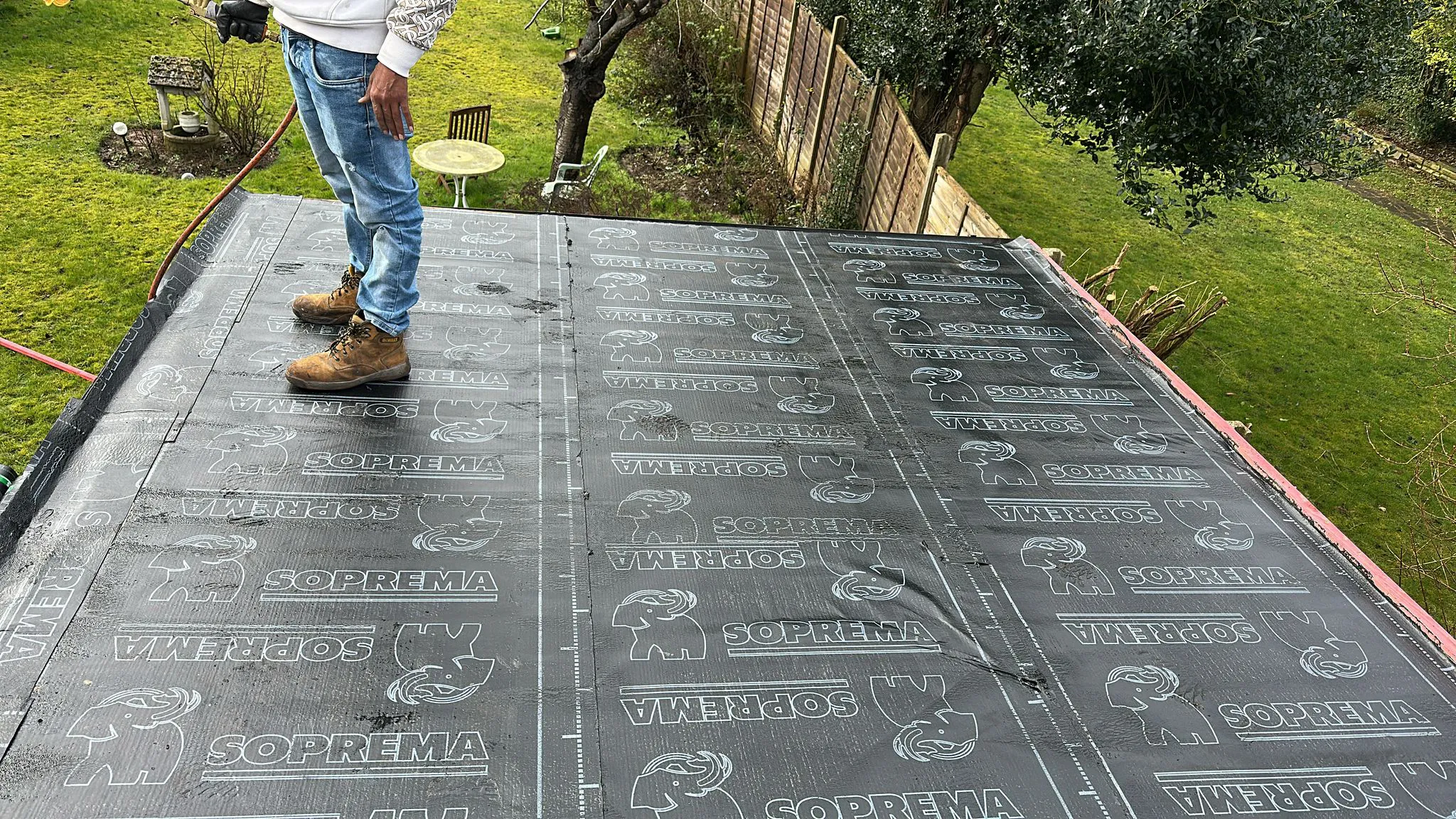 Roofer standing on newly laid torch-on felt membrane during a flat roof installation in Plymouth